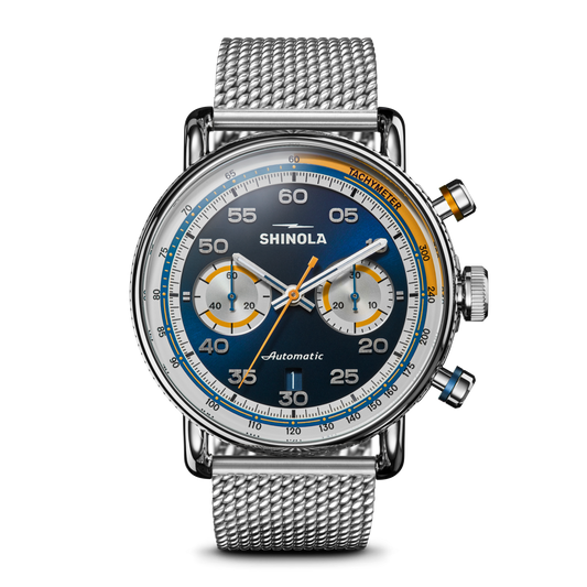 The Shinola Canfield Speedway Open Road Automatic Chronograph Watch features a blue gradient dial with two subdials, orange and blue accents, a tachymeter bezel, Swiss movement, silver mesh band, and elegant silver hands and hour markers.