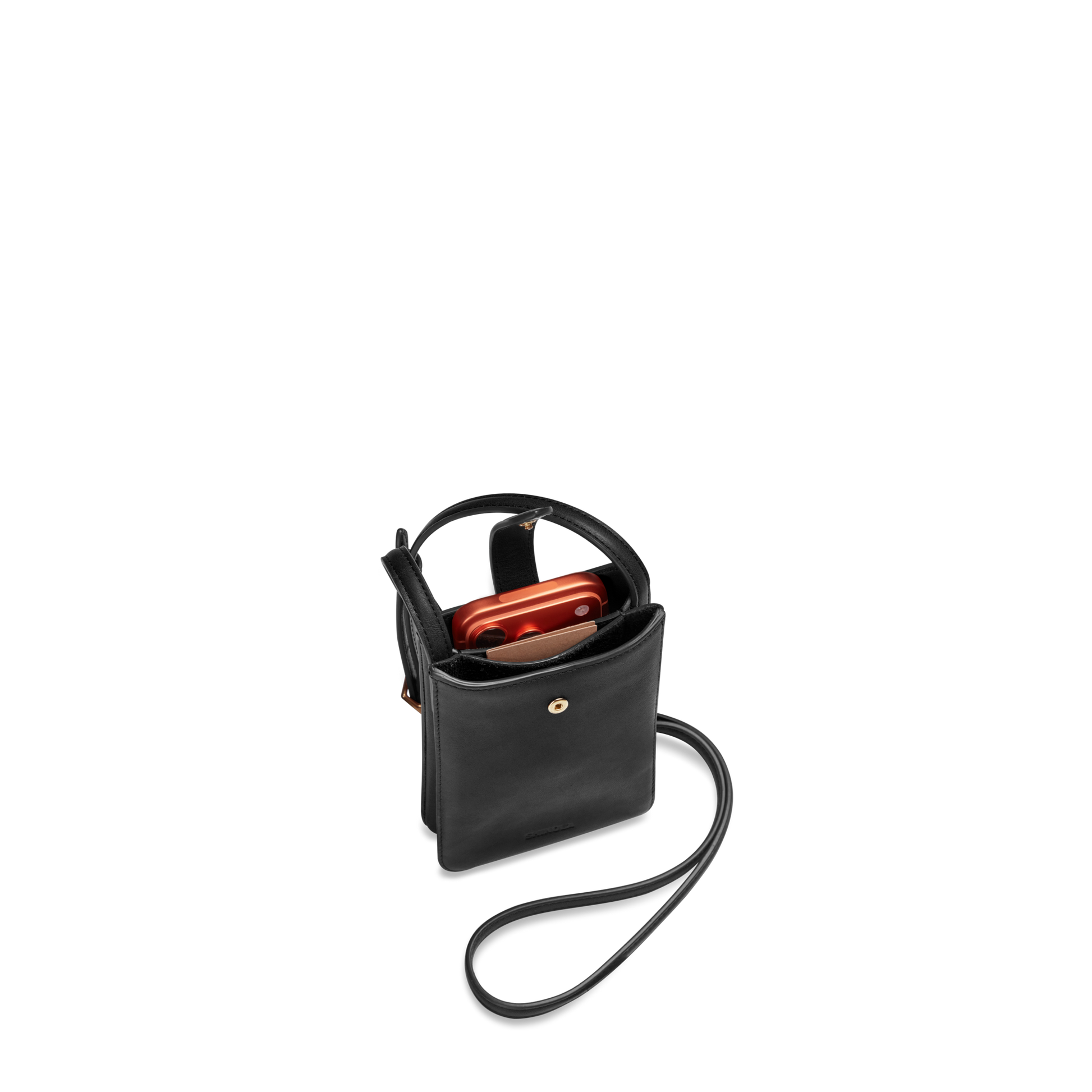 The Shinola Bixby Phone Crossbody - Black, a compact natural leather bag with a gold snap closure, holds a red smartphone and is displayed on a plain white background.