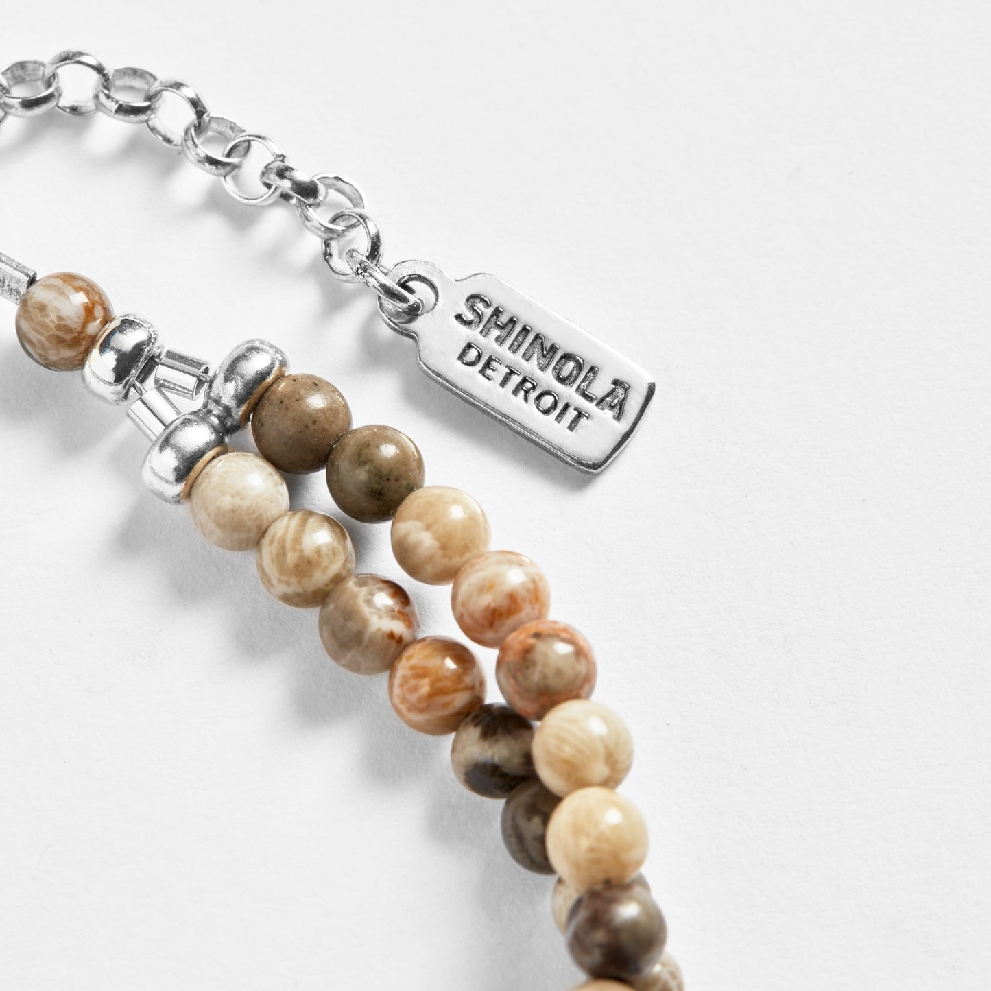 Close-up of the Shinola Double Row Petoskey Beaded Bracelet—sterling silver closure and tag engraved with Shinola Detroit, featuring round, earth-toned stones on a white background.