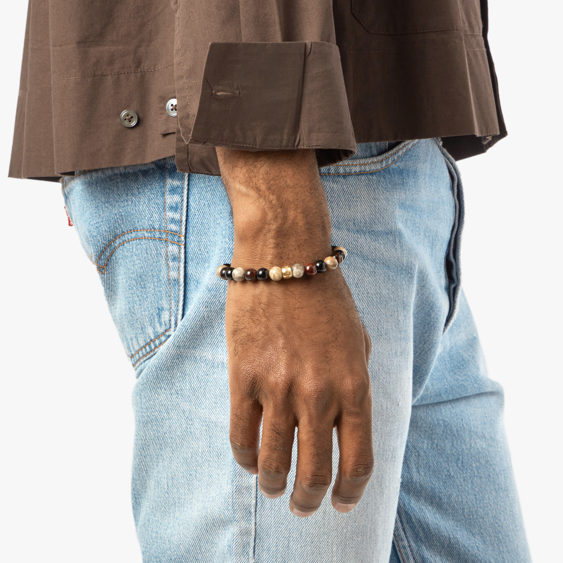 A person wearing light blue jeans, a brown shirt, and a Shinola 8mm Beaded Bracelet Multi Stone on their left wrist, with their arm relaxed by their side.