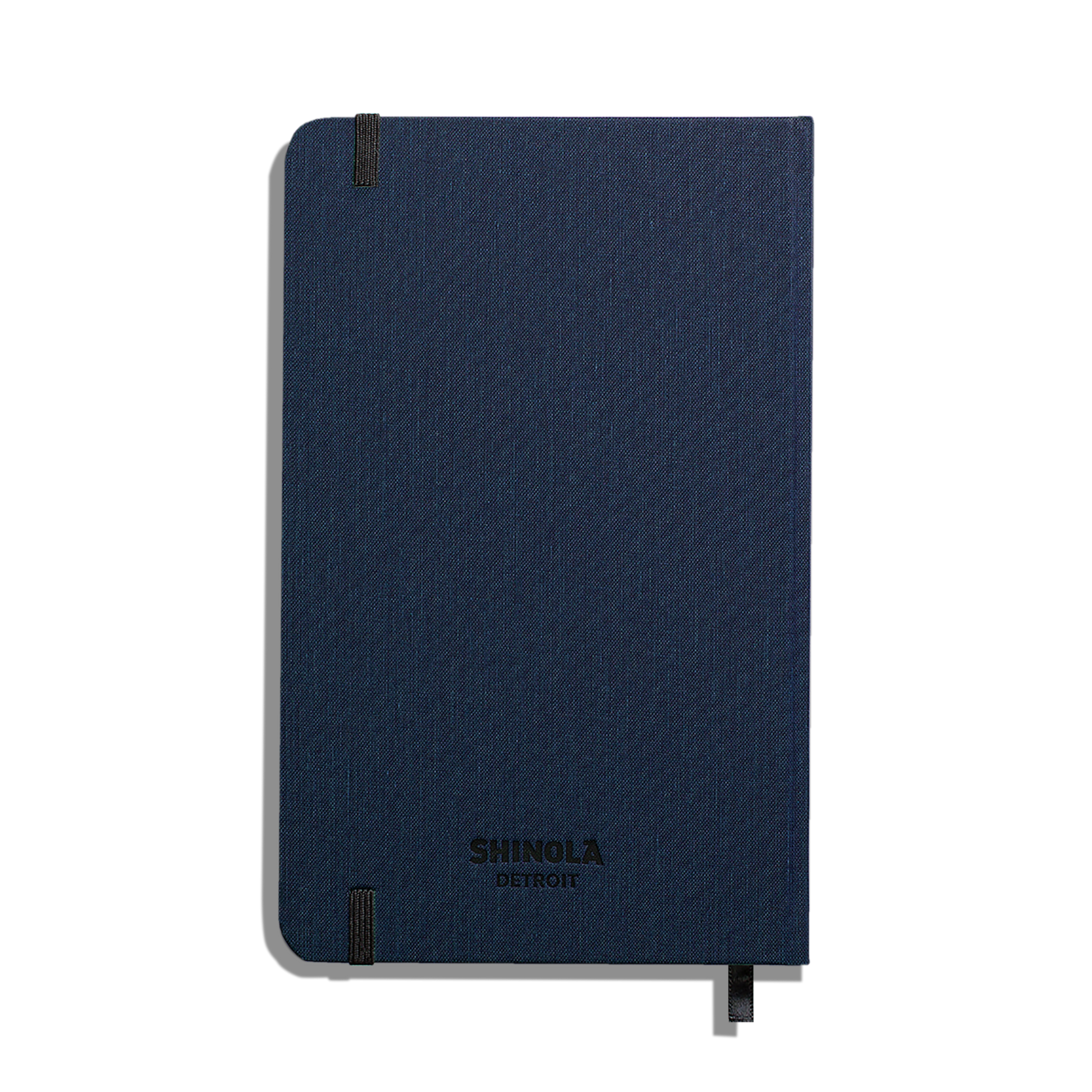 A closed Medium Hard Plain Journal - Navy by Shinola with rounded corners, an elastic band, and a ribbon bookmark is shown against a plain white background.