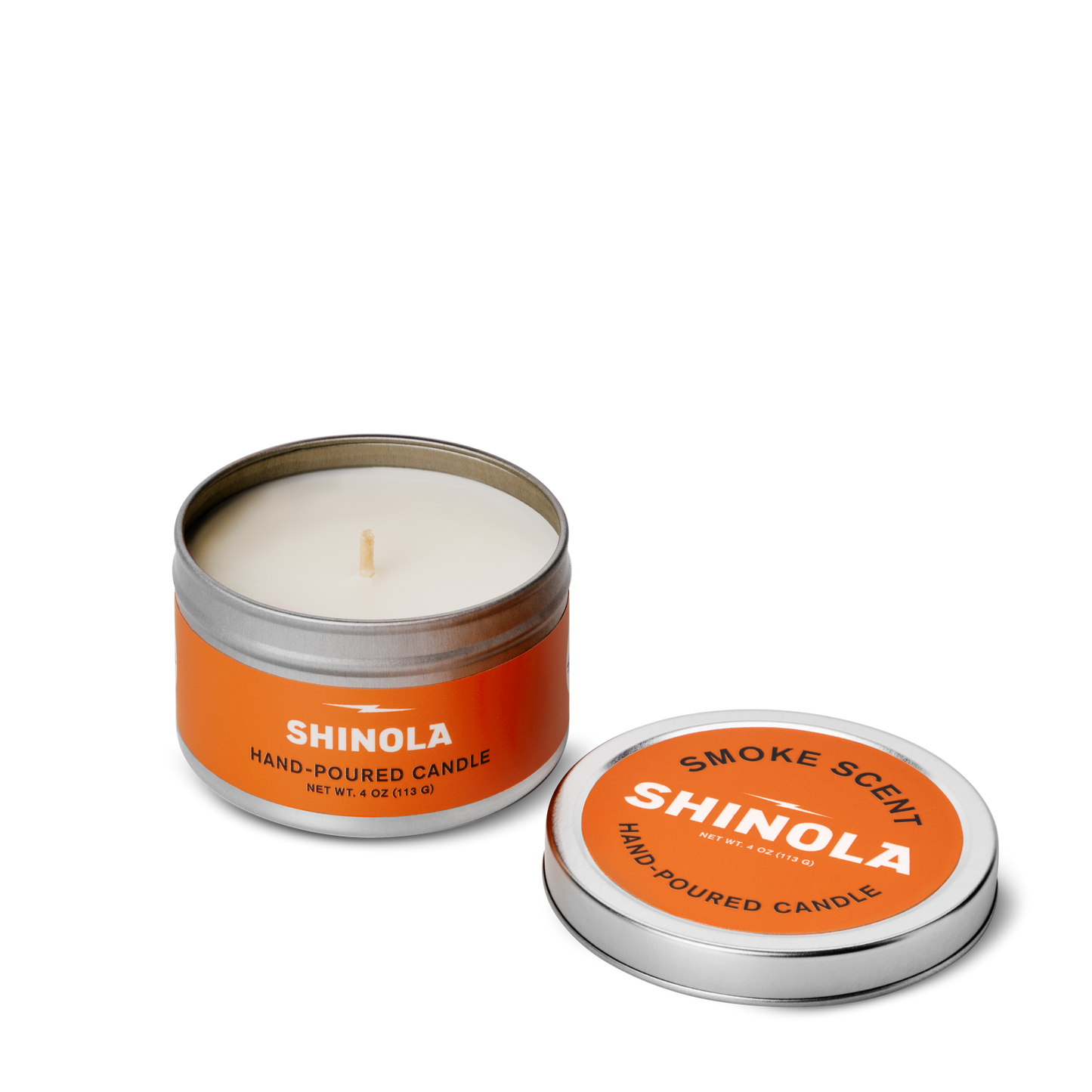 An orange tin labeled Shinola Hand Poured 4oz Travel Candle - Smoke sits open, showing a white coconut soy wax candle inside, with its lid beside it highlighting the Smoke scent and nodding to Detroit.