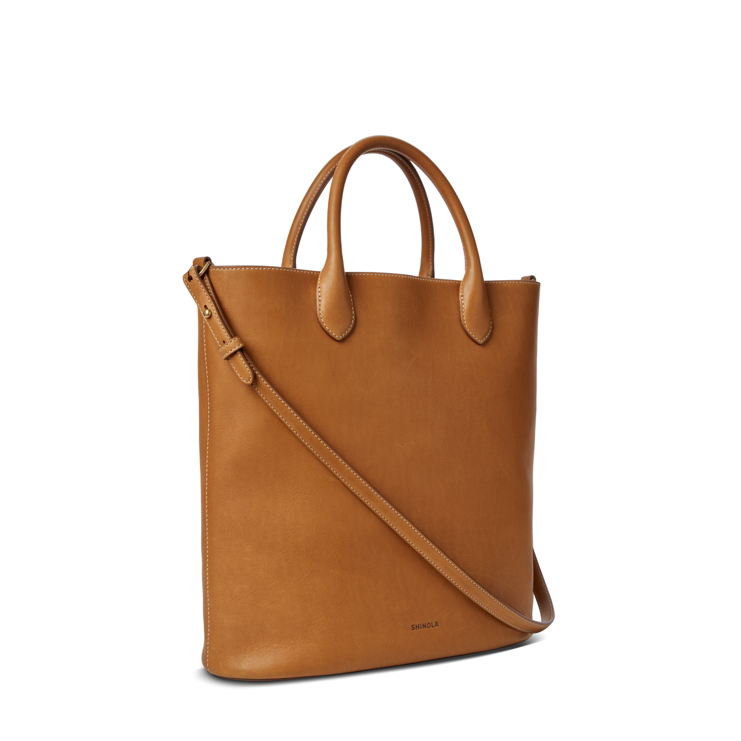 The Shinola 12 Hour Tote Bag in tan leather features two short handles, an interior pocket, and a detachable adjustable shoulder strap, shown against a plain white background.