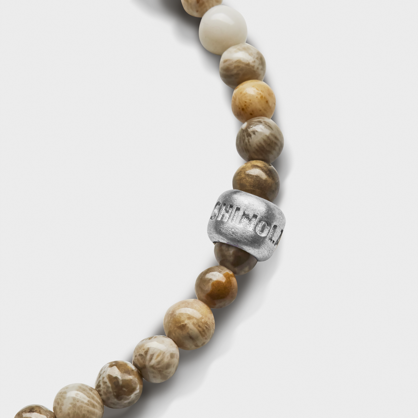A close-up of the Shinola 4mm Beaded Petoskey Bracelet, featuring round, earth-toned polished Petoskey stones and a sterling silver accent bead engraved with letters, set against a white background.
