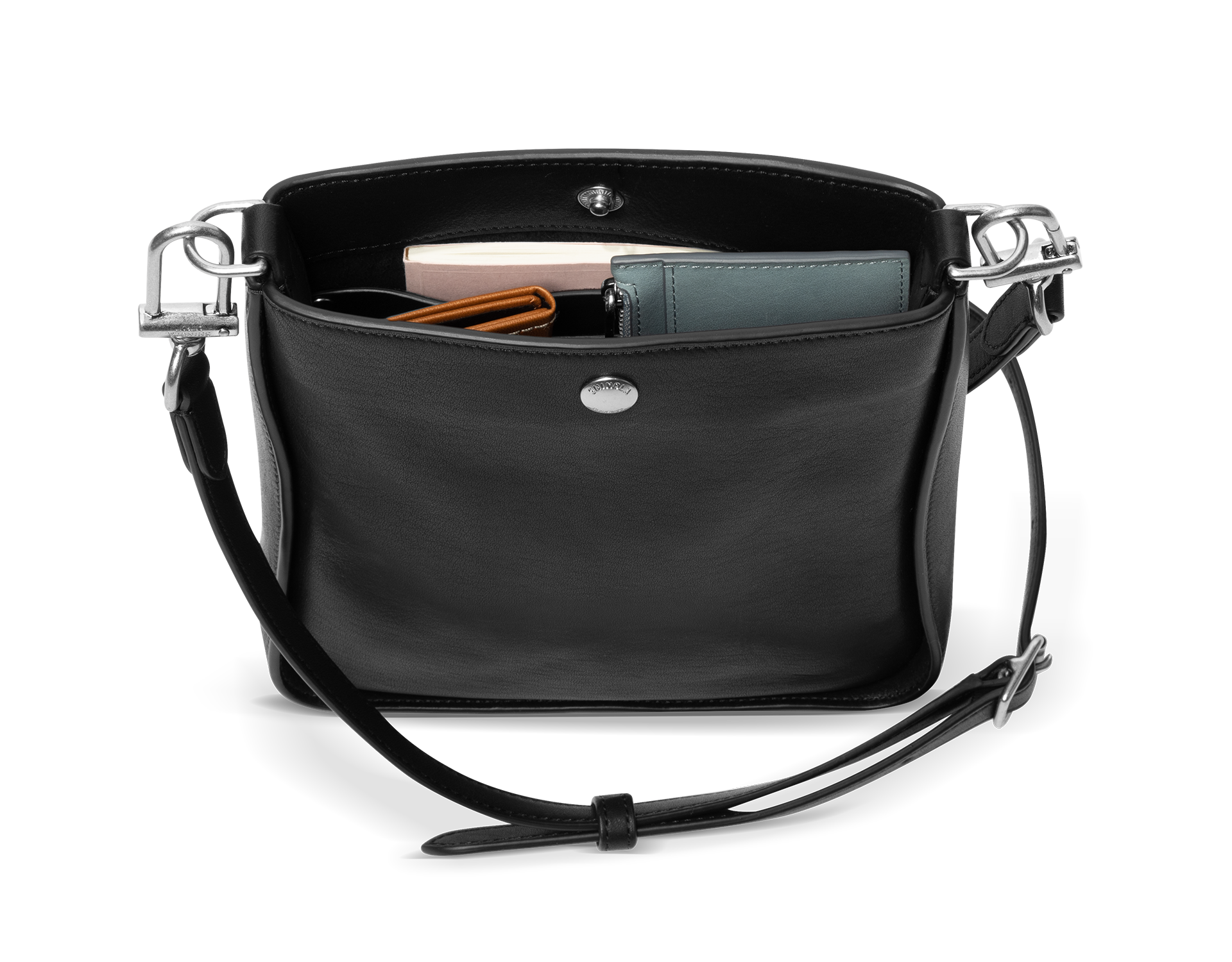 The Shinola Mini Pocket Crossbody Bag in black, shown open with a green wallet, a pink rectangular item, and an orange-striped item inside, features a snap closure and an adjustable leather strap draped in front.