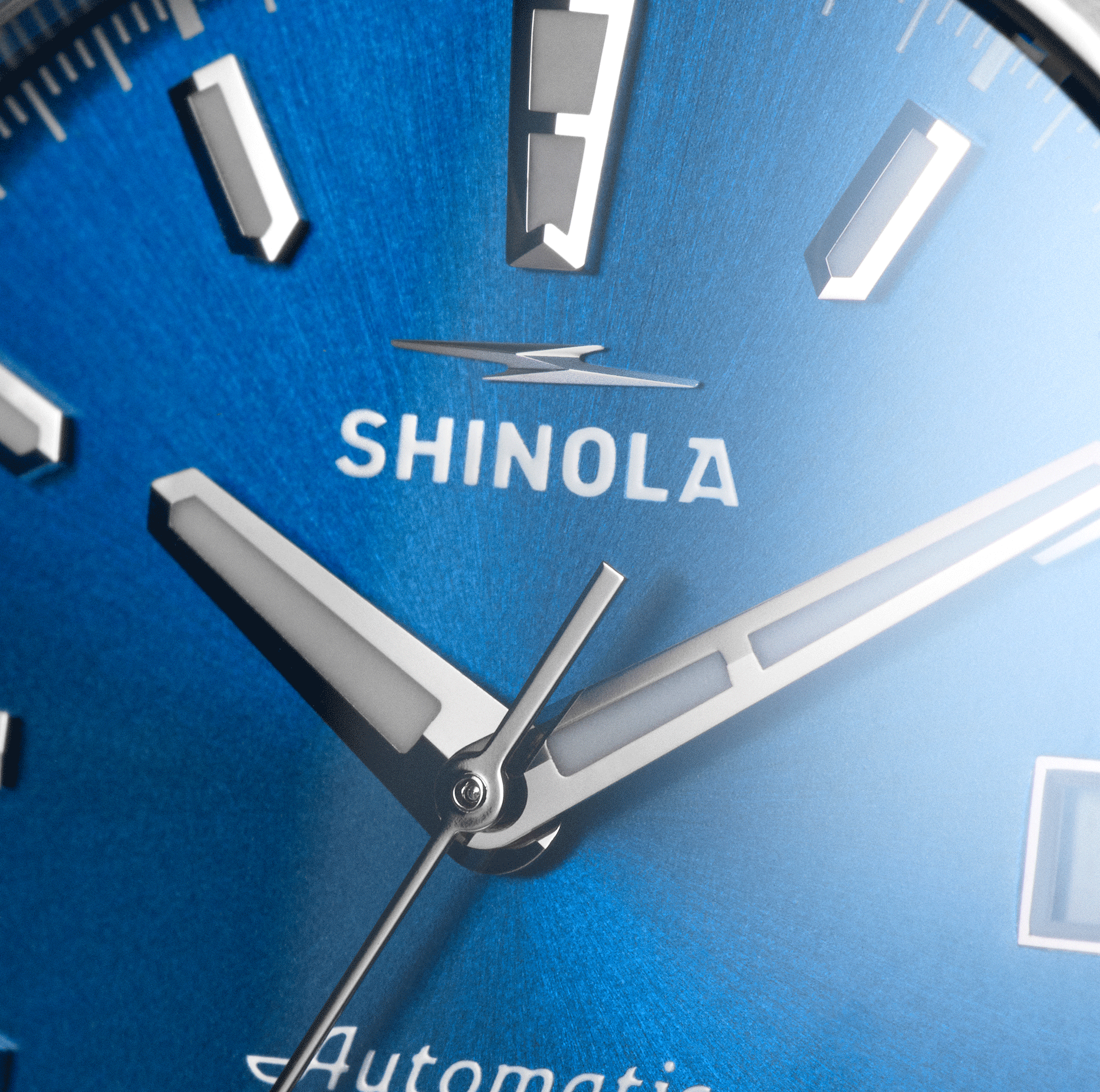 Close-up of the Shinola Circadian Monster Automatic Watch - Daylight Blue, featuring silver rectangular hour markers, hour, minute, and second hands, plus partial "Automatic" text on its striking blue face.