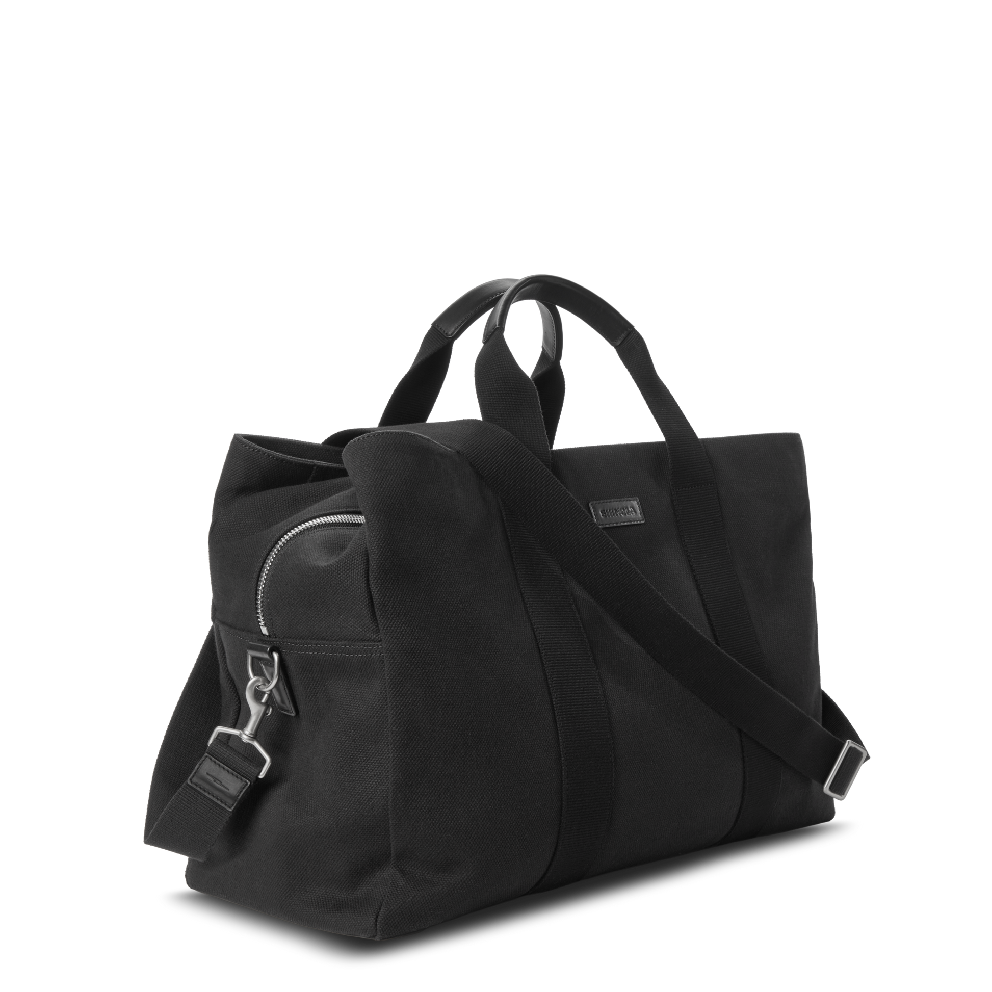 The Shinola Runwell Canvas Duffle Bag - Black features two handles, a detachable shoulder strap, front zip pocket with metal clasp, and minimalist style—ideal as a chic TSA-approved carry-on. Displayed on a plain white background.