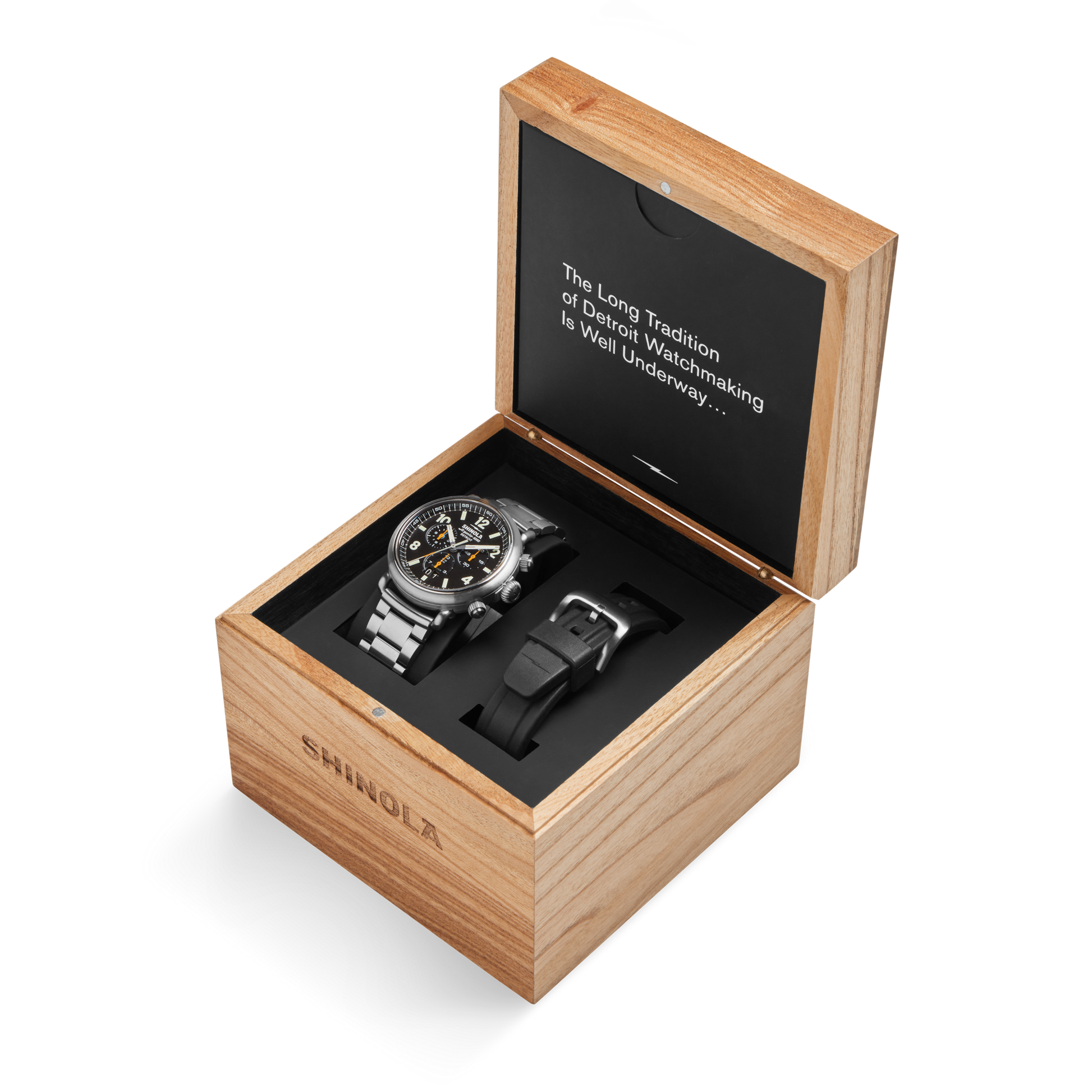 A Shinola Runwell Chronograph West Wind Watch Gift Set with an additional black strap is displayed in a wooden box with its lid open, revealing the text: "The Long Tradition of Detroit Watchmaking Is Well Underway…".