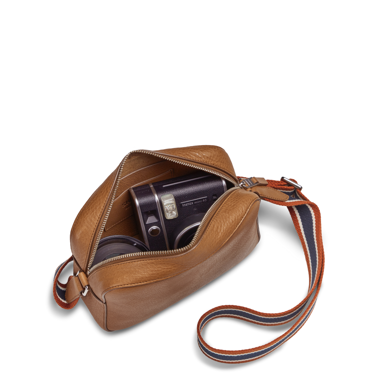 The Shinola Camera Crossbody Bag - Tan, featuring a striped adjustable strap, is open to show a vintage camera and hard case inside, all set against a plain white background.