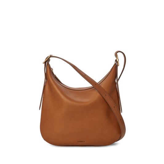 The Shinola Medium Bixby Crossbody - Tan features brown natural leather, a curved top, adjustable strap, and minimal design—versatile and perfectly displayed against a plain white background.