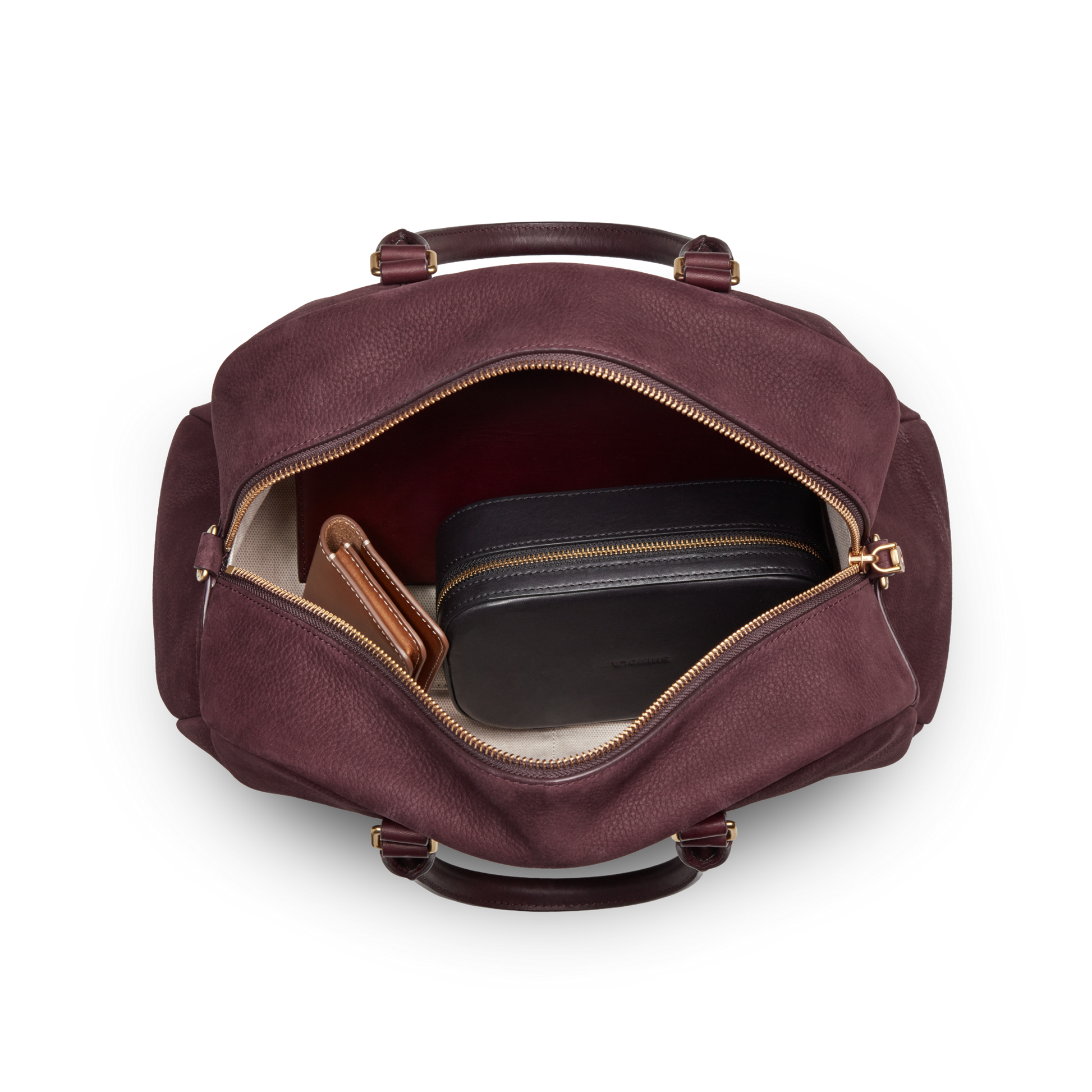 A top-down view of an open Shinola Runwell Satchel - Merlot with gold zippers reveals a brown wallet and a black zippered pouch inside, all set against a white background.