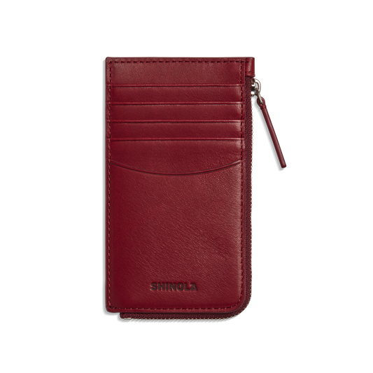 The Shinola Zip Around Card Case - Ruby features natural burgundy leather, several card pockets, a right zippered coin pocket, and "Shinola" embossed at the bottom.