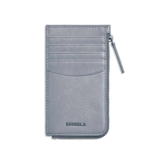 The Zip Around Card Case - Mist by Shinola is a slim, light gray leather case with five card pockets, a right-side zippered pocket, and the Shinola name embossed at the bottom.