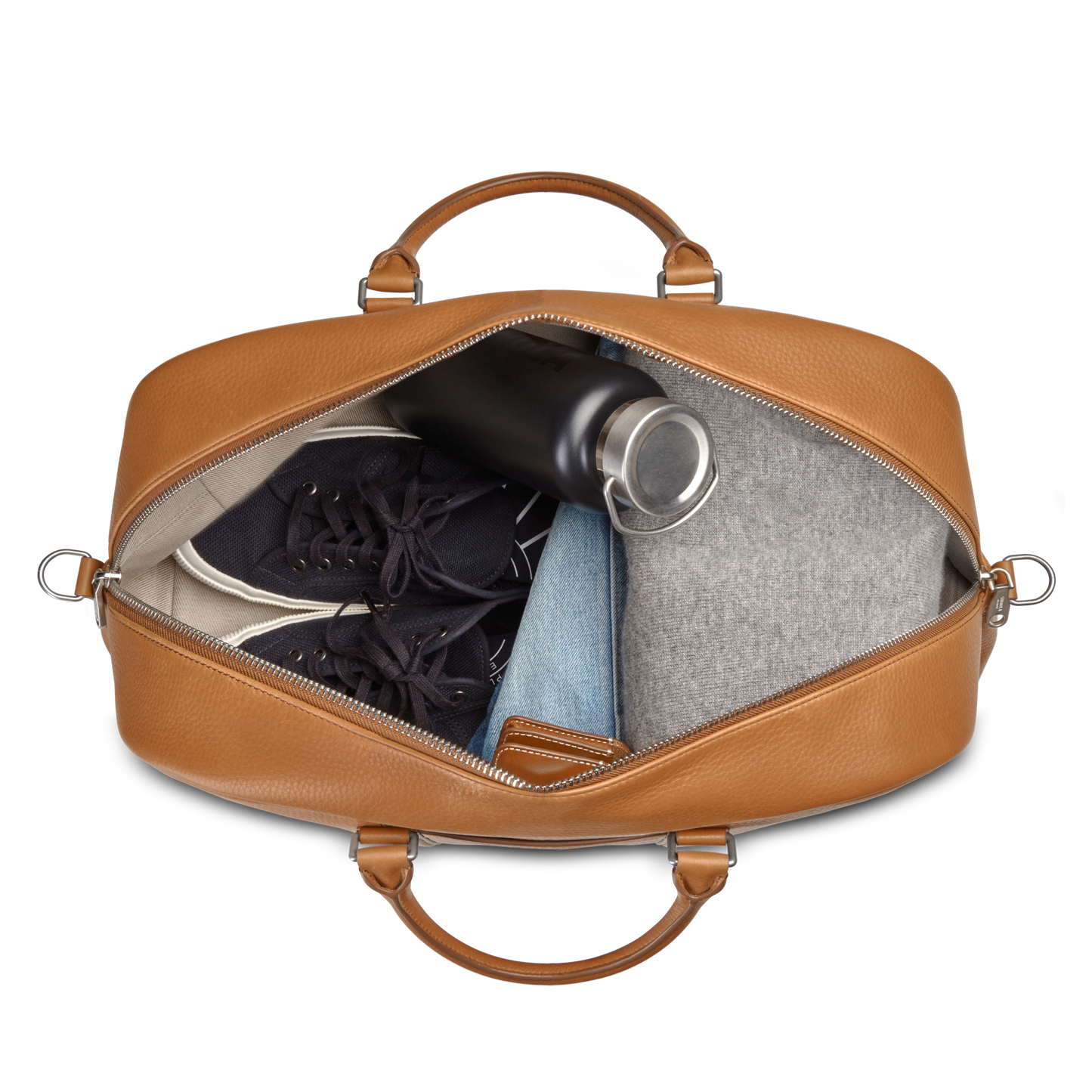 A top-down view of an open Shinola Runwell Duffle Bag in tan, TSA carry-on size, packed with black sneakers, a black water bottle, a folded gray garment, and light blue folded jeans.