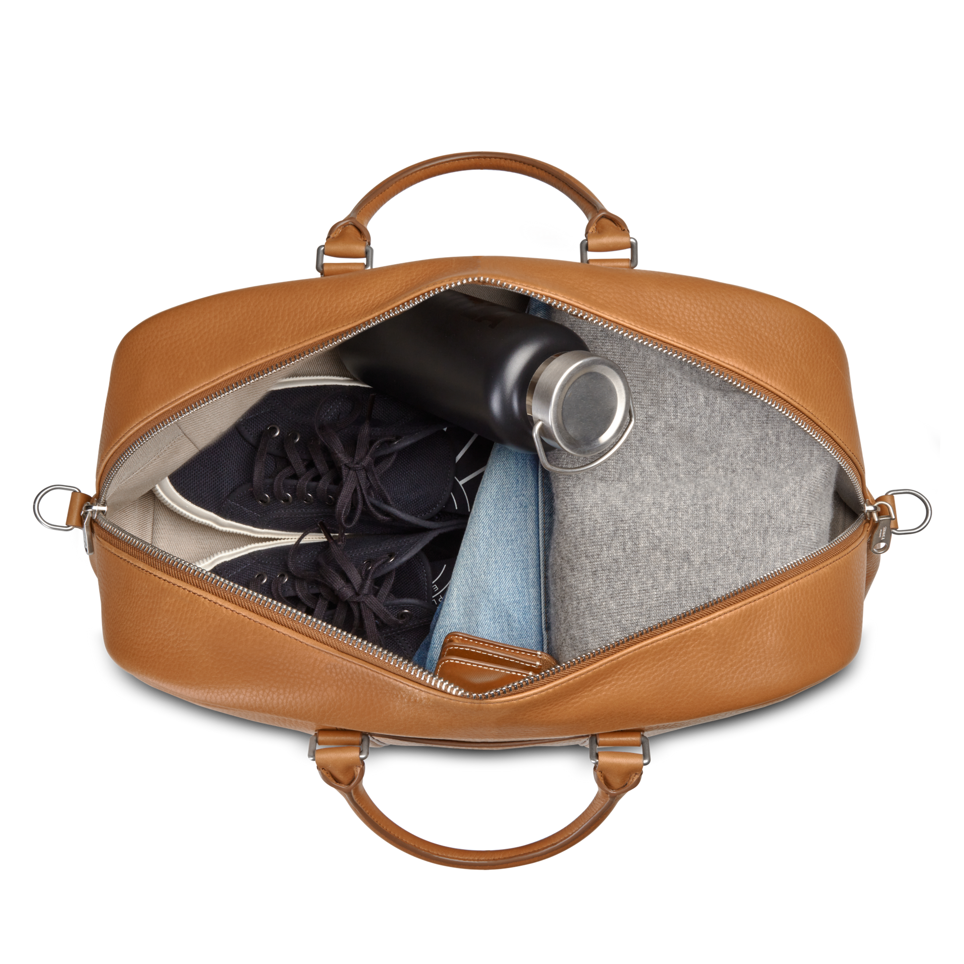 A top-down view of an open Shinola Runwell Duffle Bag in tan, TSA carry-on size, packed with black sneakers, a black water bottle, a folded gray garment, and light blue folded jeans.