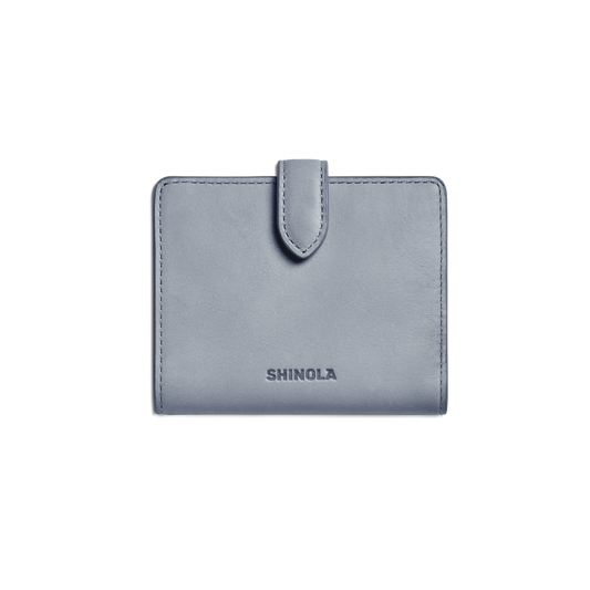 A closed Small Snap Wallet - Mist by Shinola, featuring a light blue color and tab closure with the brand name embossed on the front, is shown against a plain white background.