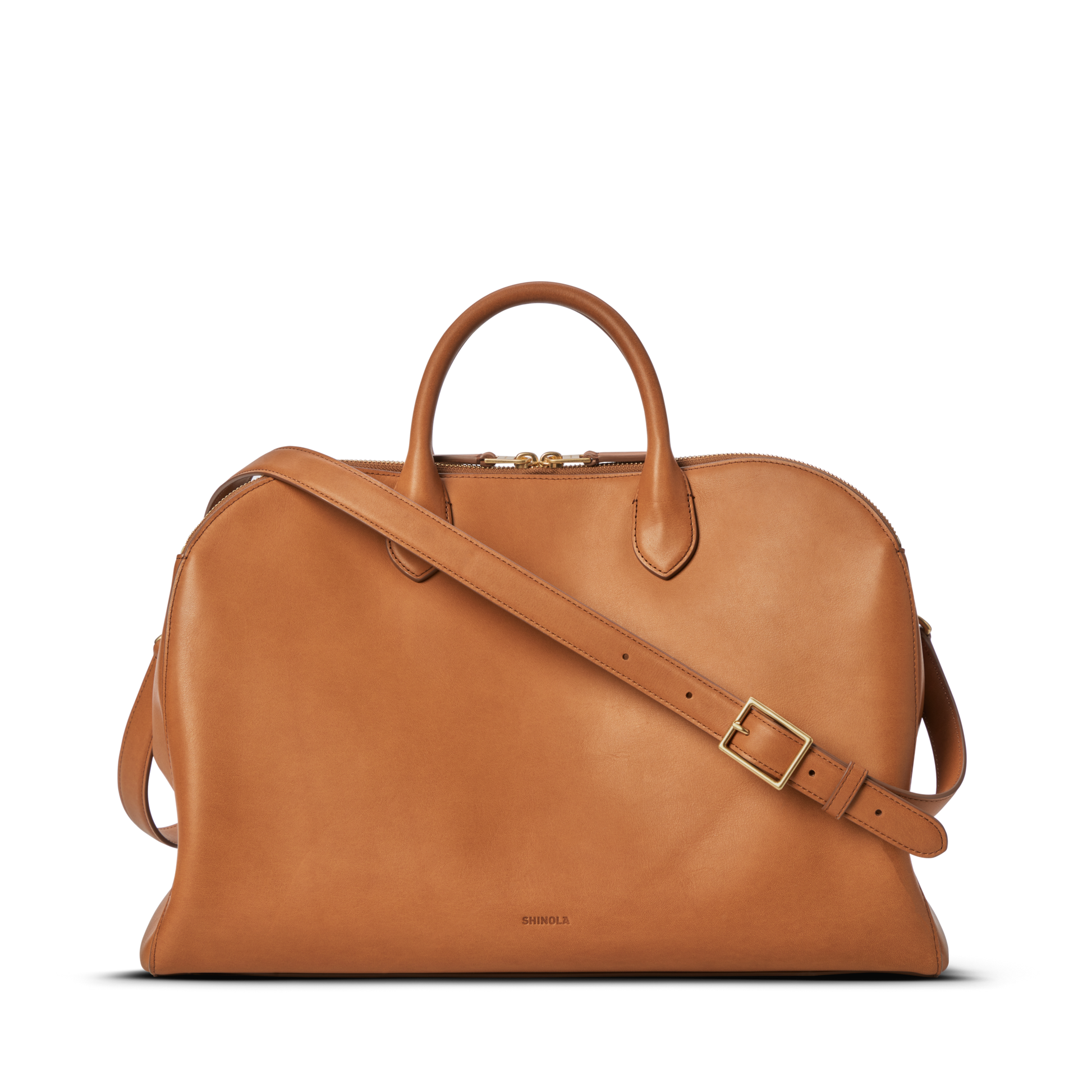 The Shinola Bixby Work Satchel - Tan is crafted in natural leather with two handles, a detachable shoulder strap, gold-tone hardware, and a small embossed logo near the bottom center, shown on a plain white background.