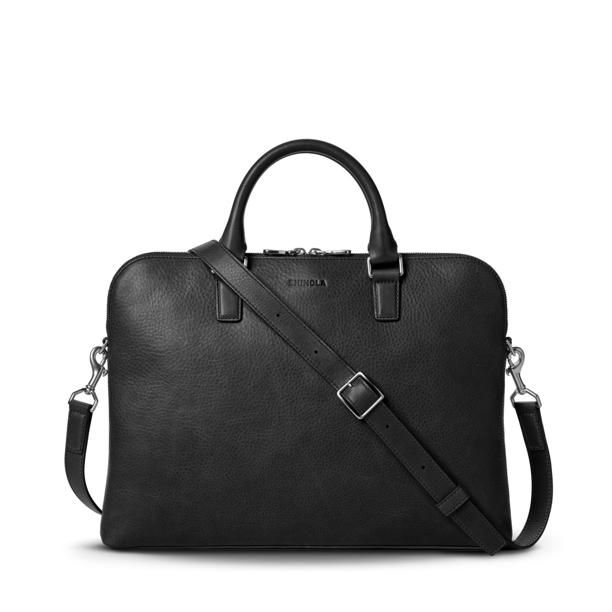 The Shinola Portfolio Briefcase in black features European grain leather, two handles, a detachable shoulder strap, silver hardware, zipper closure, and an embossed Shinola logo near the top center.
