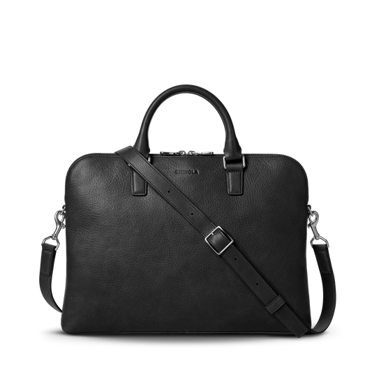 The Shinola Portfolio Briefcase in black features European grain leather, two handles, a detachable shoulder strap, silver hardware, zipper closure, and an embossed Shinola logo near the top center.