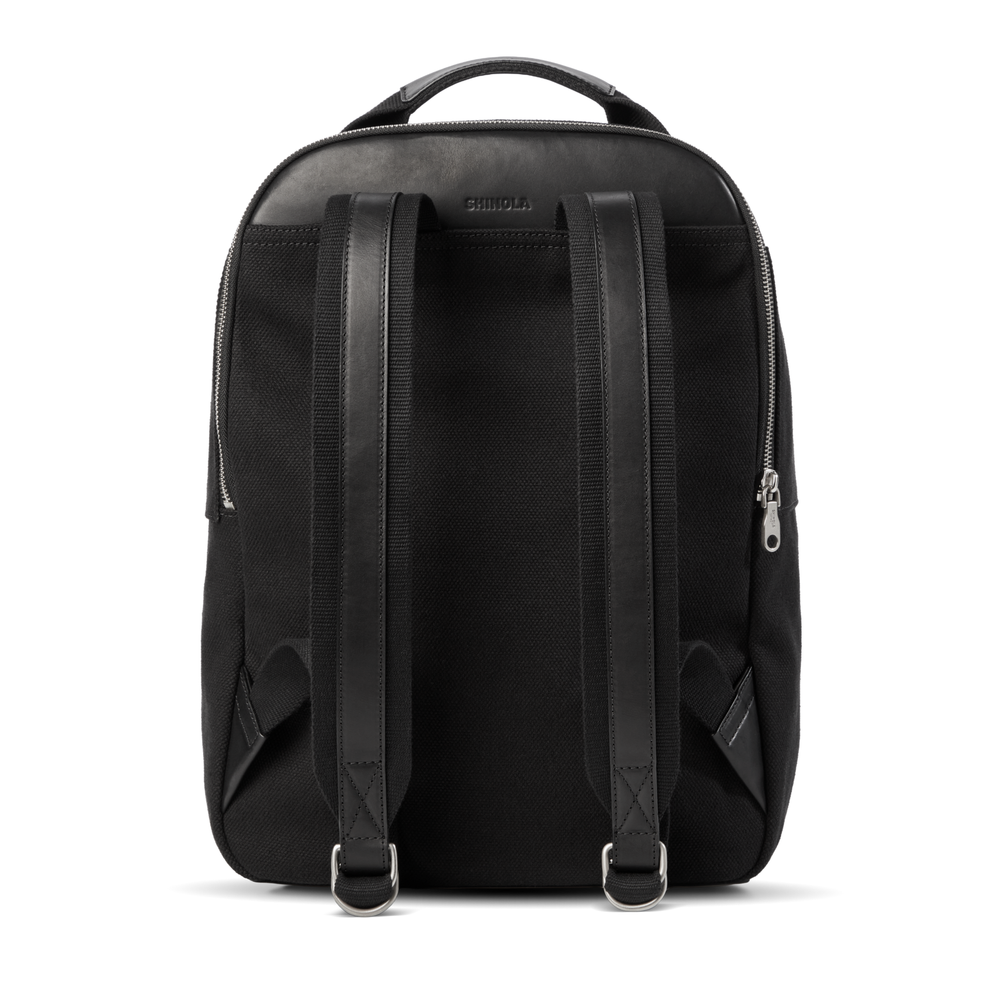 The Shinola Runwell Canvas Backpack in black is shown from the back, featuring leather accents, adjustable padded straps, metal buckles, a top handle, and visible side zippers—ideal for everyday use or adventure.