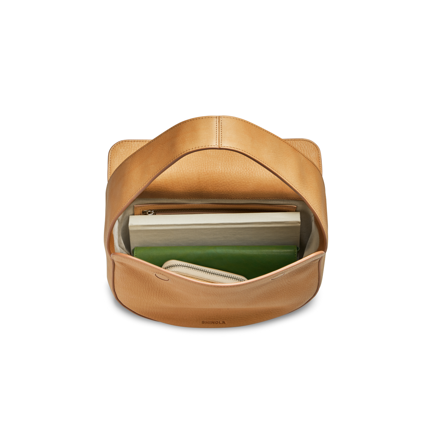 The Small Shoulder Bag - Honey by Shinola, crafted from natural grain leather, is open to show a closed laptop, green notebook, and beige book neatly inside. Its wide strap and compact size blend style with everyday practicality.