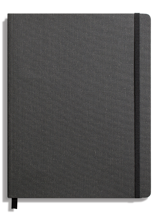 The Shinola Large Soft Ruled Journal in Charcoal features a textured fabric cover, smyth-sewn binding for durability, a black elastic closure on the right side, and a black ribbon bookmark at the bottom.