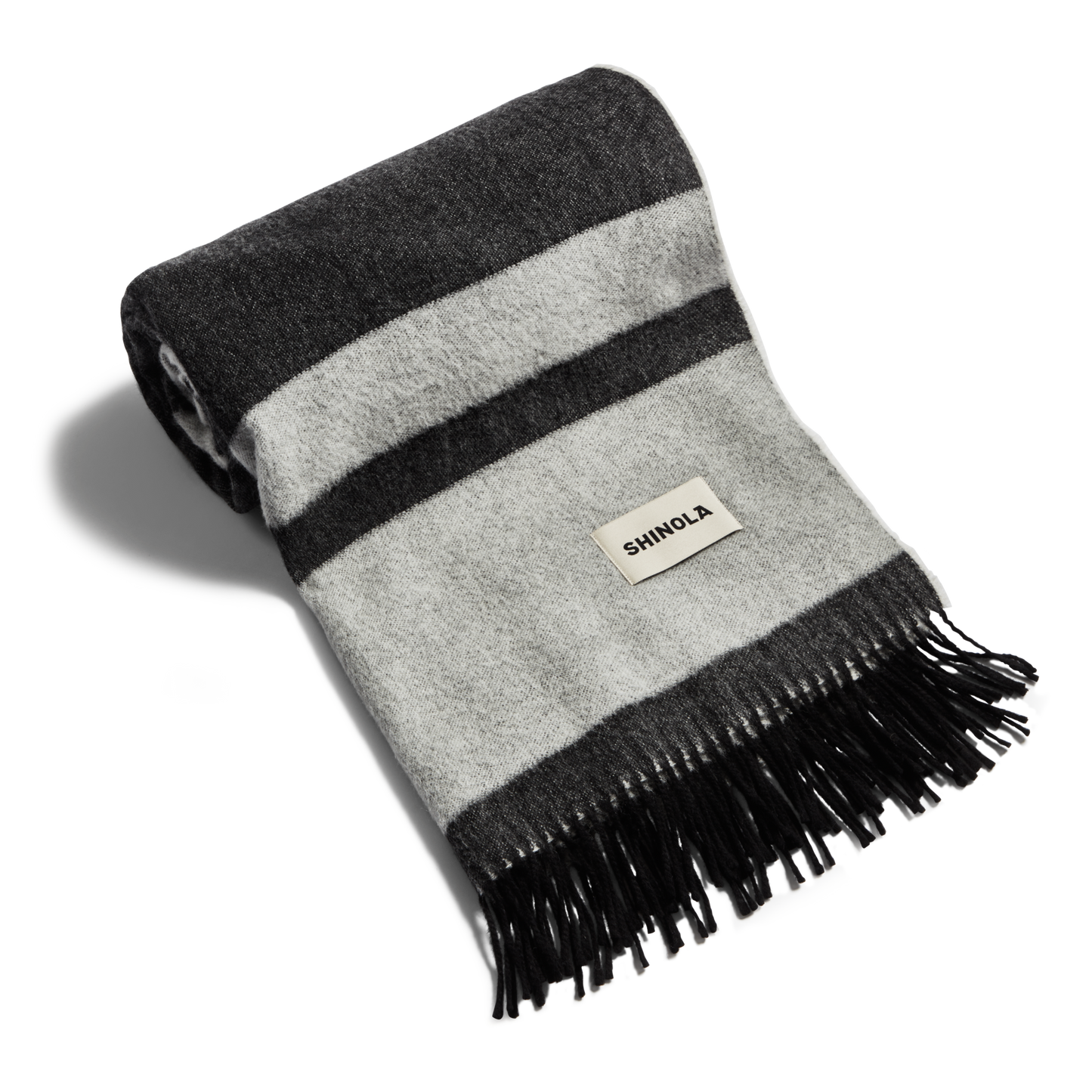 The Shinola Woven Alpaca Wool Blanket features horizontal dark and light gray stripes, black fringe ends, and a sewn-on Shinola label.