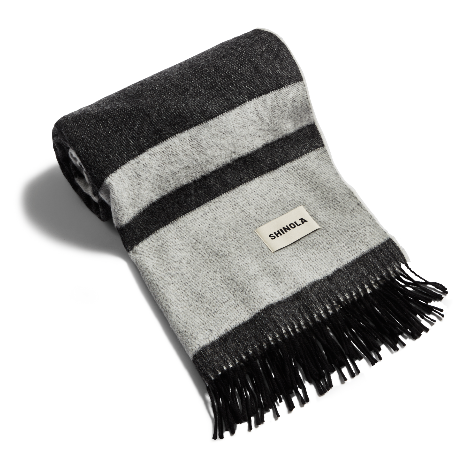The Shinola Woven Alpaca Wool Blanket features horizontal dark and light gray stripes, black fringe ends, and a sewn-on Shinola label.