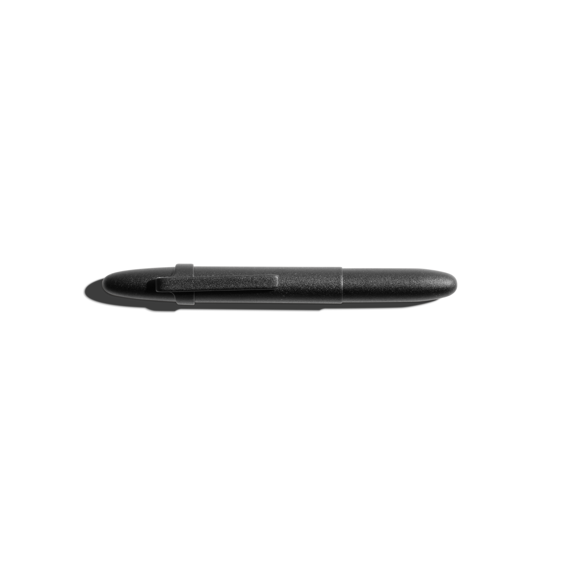 A Shinola + Fisher Bullet Space Pen - Matte Black with a clip rests horizontally on a white surface, casting a shadow to the left. This Shinola pen writes underwater and in extreme conditions.