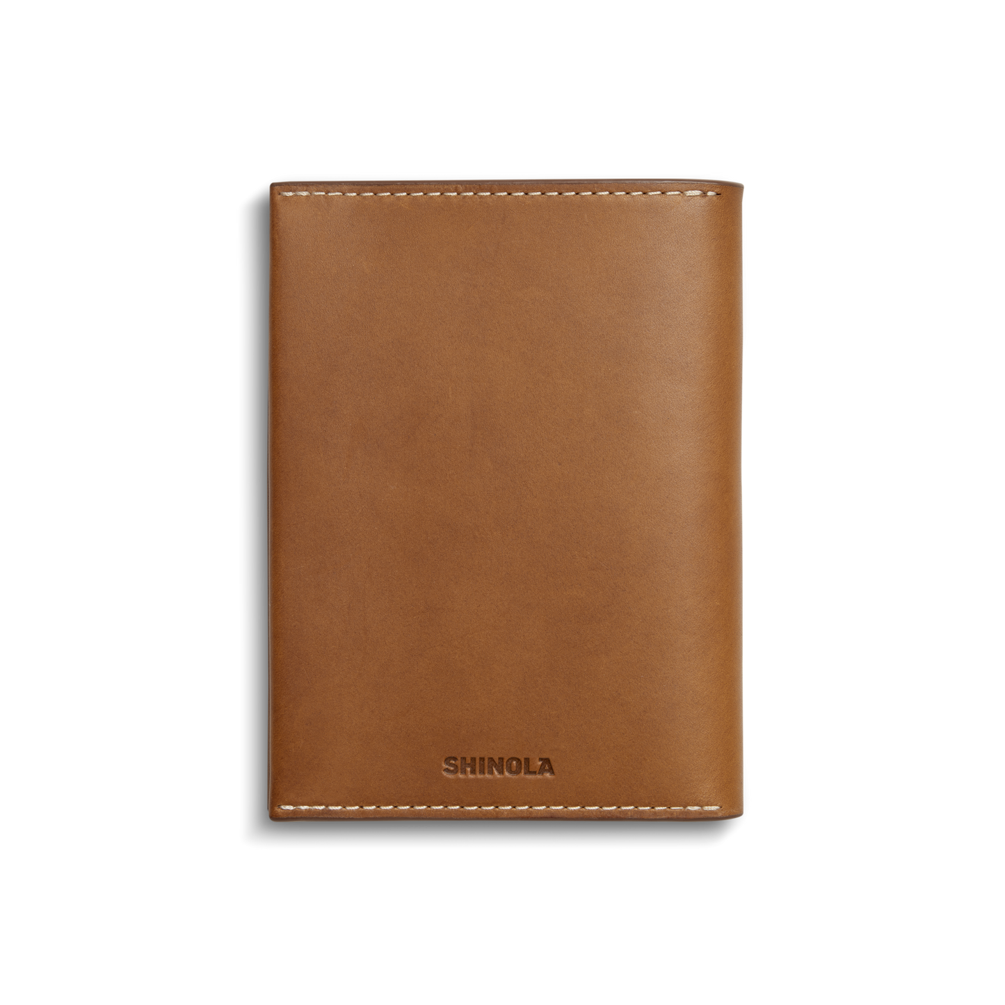 A closed, tan Shinola Passport Holder with white stitching and the brand embossed at the bottom center, displayed on a plain white background—a refined travel accessory.