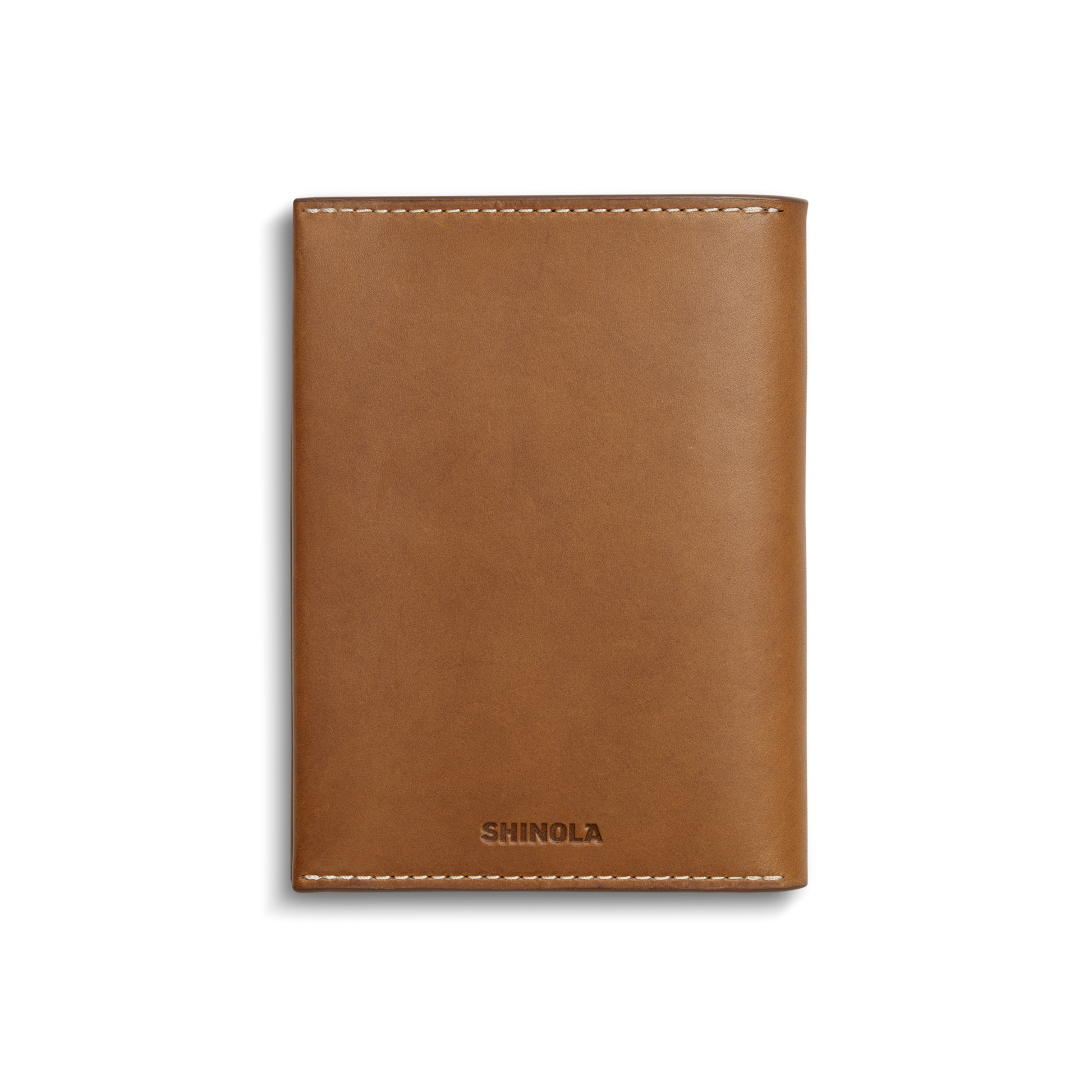 A closed, tan Shinola Passport Holder with white stitching and the brand embossed at the bottom center, displayed on a plain white background—a refined travel accessory.