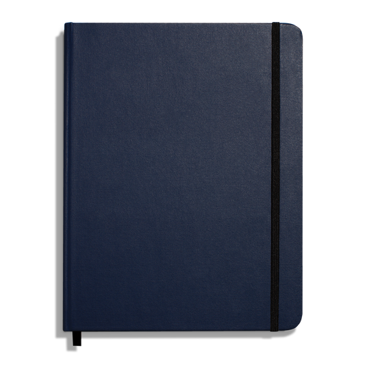 The Shinola Large Hard Ruled Journal in Navy features a closed hard linen cover, a black elastic band along the right edge, and a black ribbon bookmark visible at the bottom.