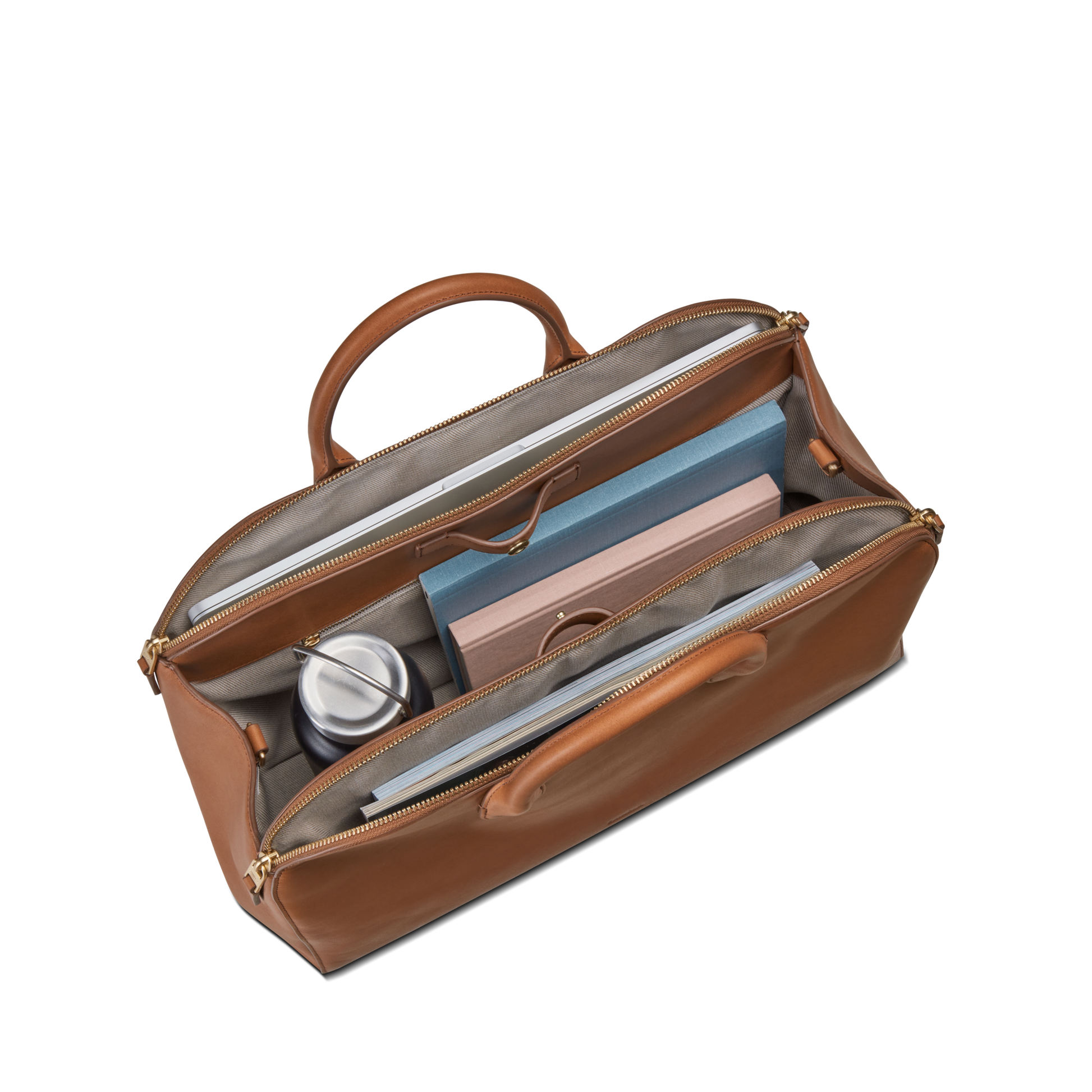 The Shinola Bixby Work Satchel - Tan features two handles and organized compartments, holding a metal tumbler, pink notebook, blue folder, and small items—making it a stylish laptop bag against a white background.