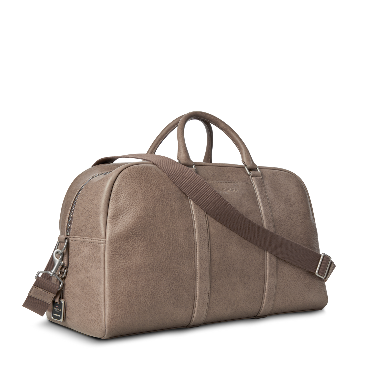 The Shinola Runwell Duffle Bag - Stone is crafted from natural grain leather in taupe, featuring dual handles, a detachable brown shoulder strap, and a zipper closure, displayed on a plain white background.