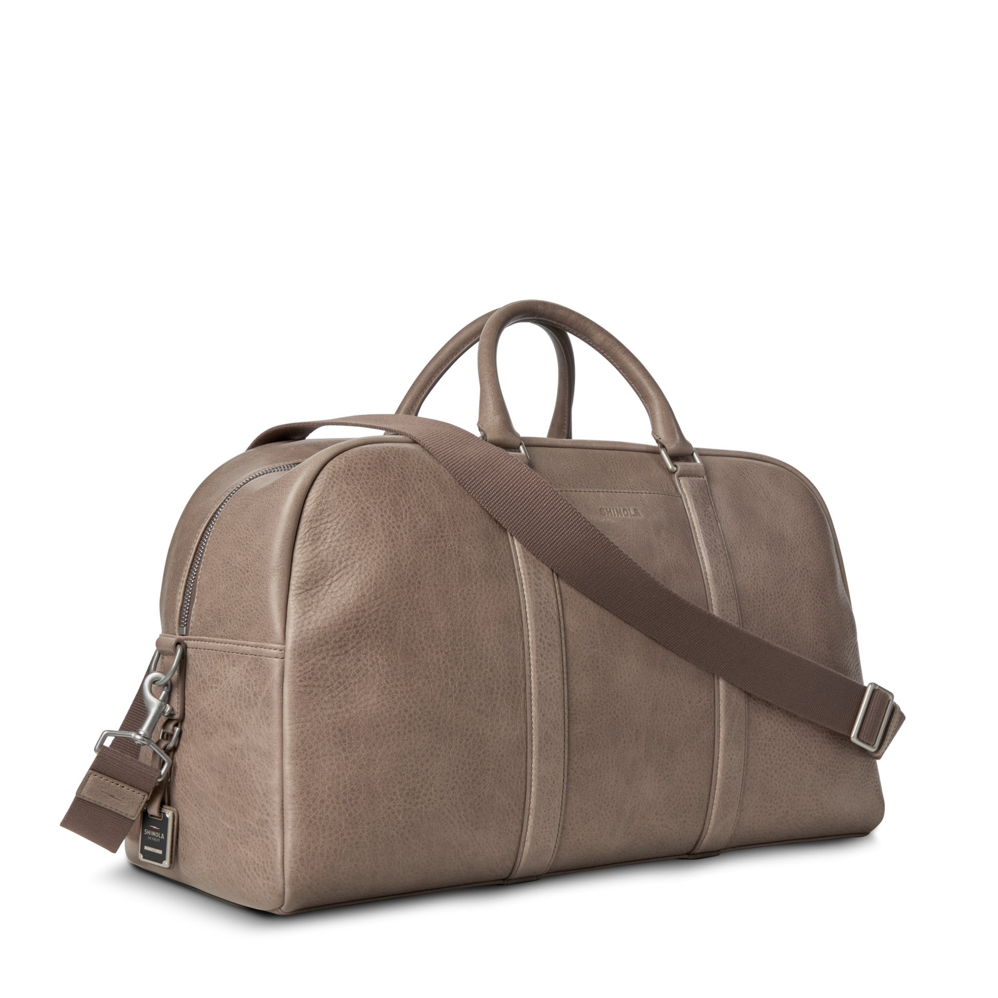The Shinola Runwell Duffle Bag - Stone is crafted from natural grain leather in taupe, featuring dual handles, a detachable brown shoulder strap, and a zipper closure, displayed on a plain white background.