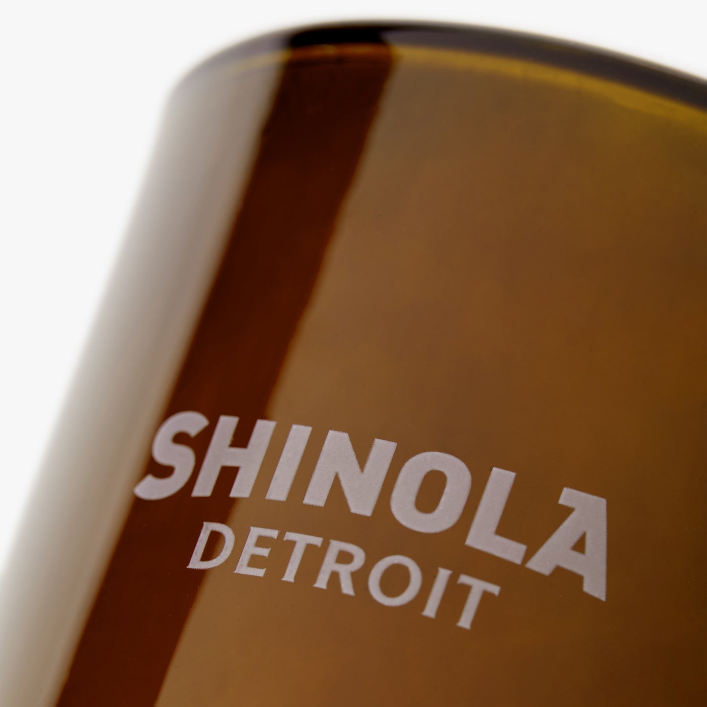 Close-up of the Shinola Smoke 8oz Scented Candle in a brown glass featuring white "SHINOLA DETROIT" text, emphasizing the brand, smooth texture, and evoking a cozy Detroit fall candle experience.