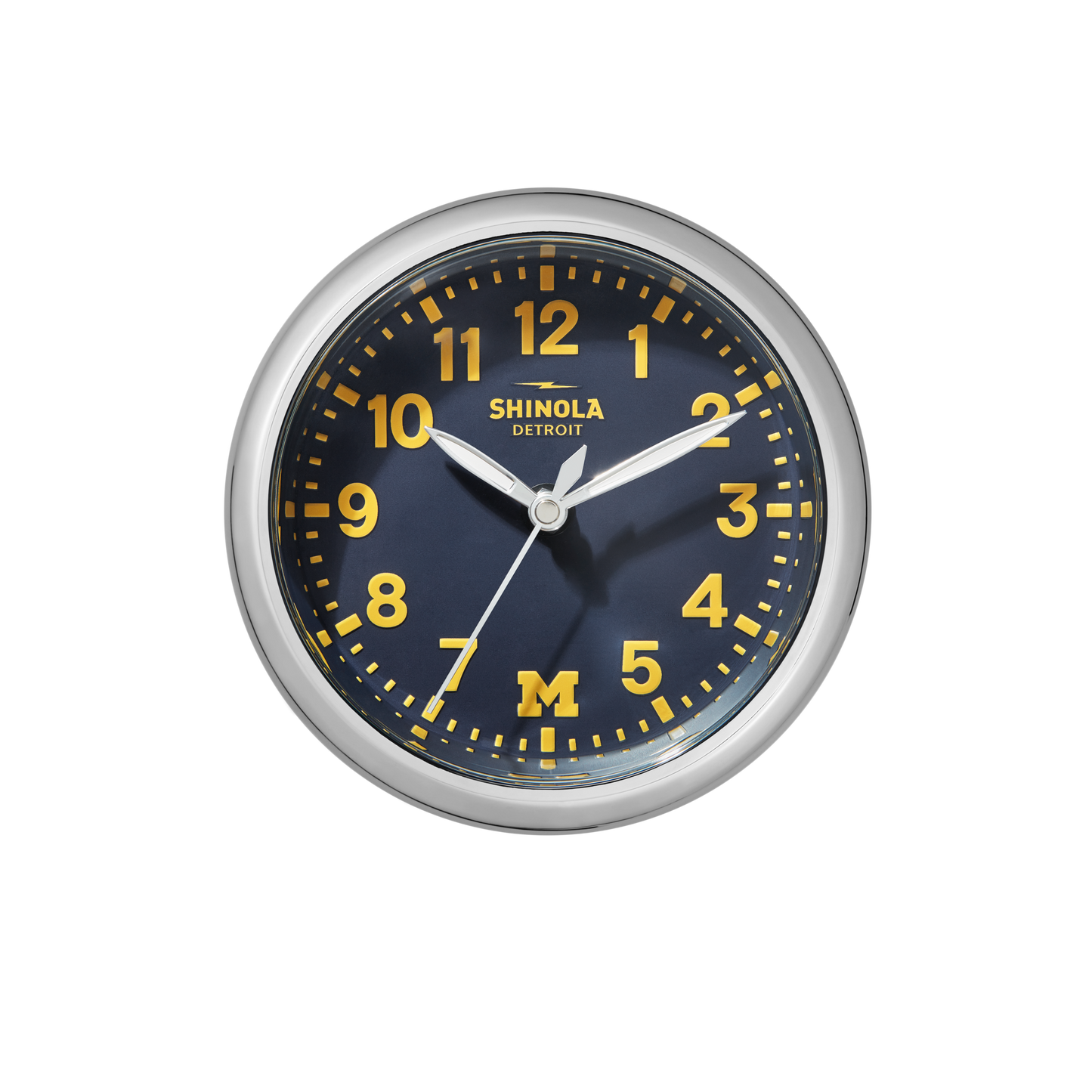 The 6" Runwell Clock - Blue by Shinola features a round silver frame, wolverine blue face, yellow numbers and hands, and displays 1:12. The clock face is inspired by the University of Michigan with "Shinola Detroit" and a yellow M printed on it.