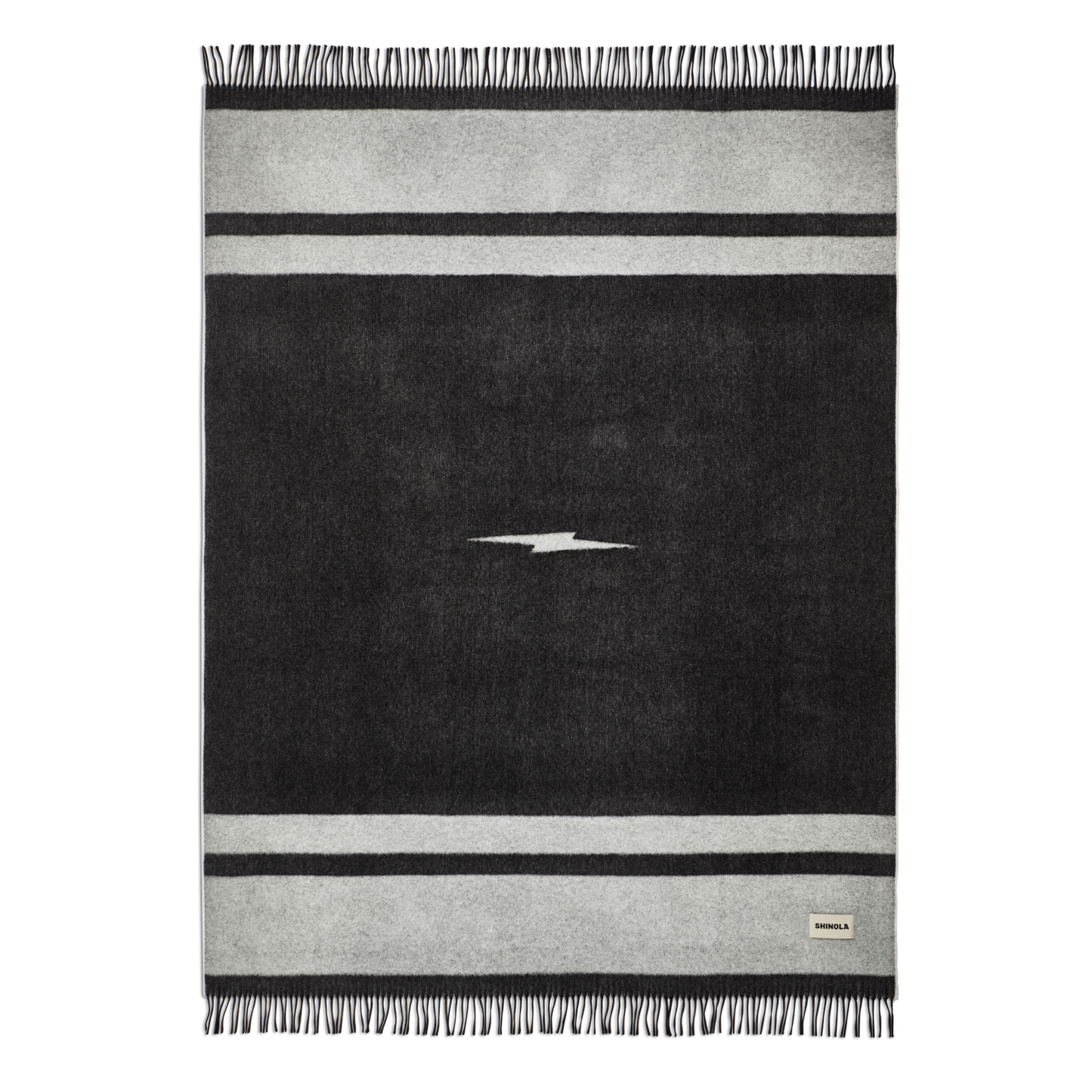 The Shinola Woven Alpaca Wool Blanket is a handcrafted black and gray rectangular throw from Peru, featuring a central white lightning bolt, two horizontal gray stripes, fringe on the short edges, and a small corner fabric label.