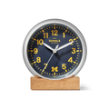 The 6" Runwell Clock - Blue by Shinola is a round analog desk clock with a wolverine blue face, yellow numbers and hands, the letter M at the bottom, Shinola branding at the top, reads 2:10, and sits on a wooden base.