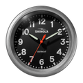 The 14" Runwell Clock by Shinola features a tumbled zinc casing, black face, white numerals, luminescent hour and minute hands, red second hand, displays 10:09:34, and showcases an industrial design.