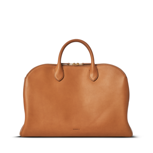 The Shinola Bixby Work Satchel - Tan is a sleek, minimalist natural leather laptop bag with two handles, zipper closure, and subtle Shinola embossing near the bottom center, shown against a plain white background.