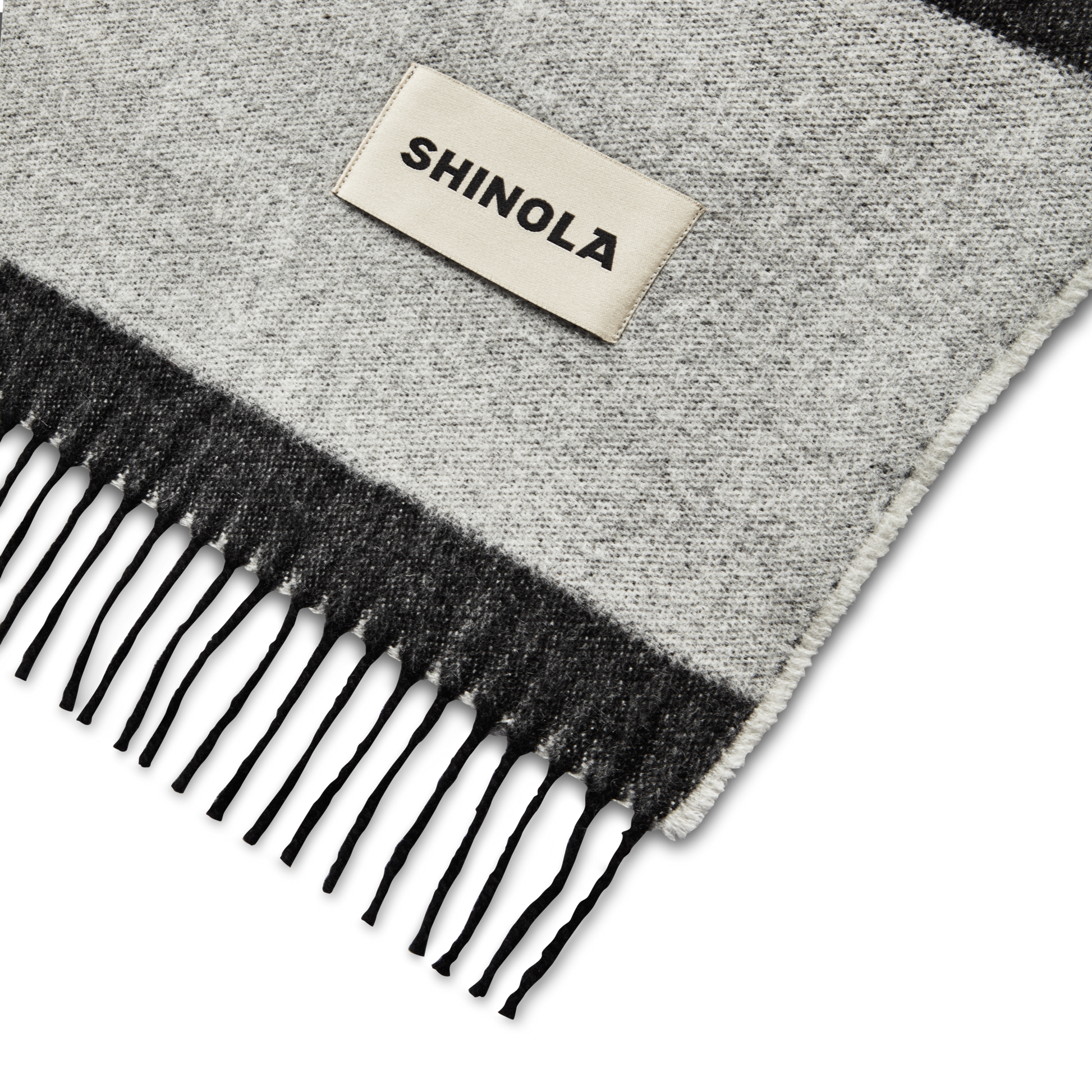 A close-up of the Shinola Woven Alpaca Wool Blanket, featuring gray and black fringes and a rectangular white Shinola patch, reminiscent of premium Peruvian craftsmanship.