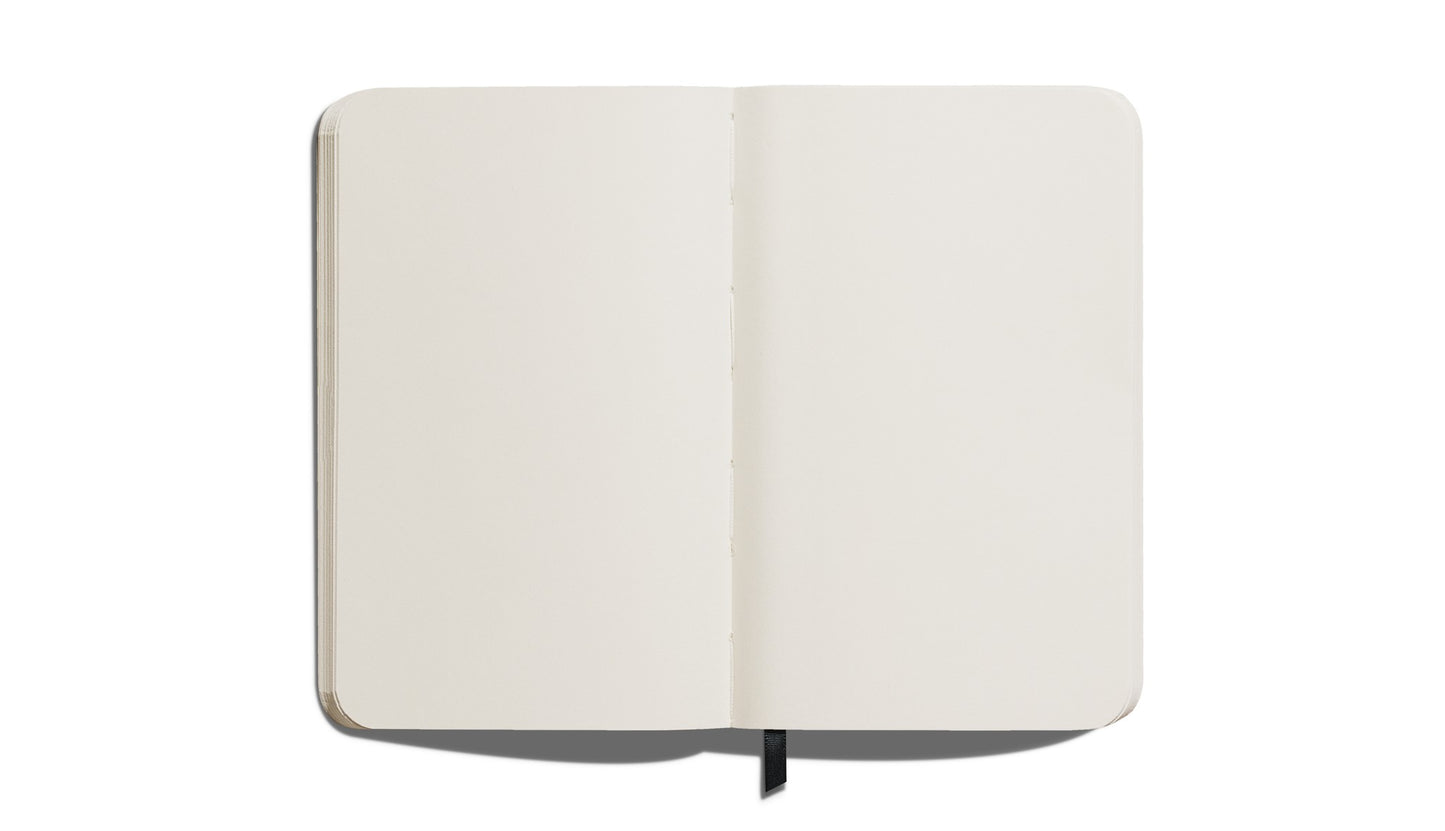 The Shinola Medium Hard Plain Journal in black features cream, acid-free pages and rounded corners. It lies flat with a black ribbon bookmark visible against a white background.