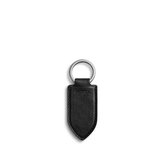 The Shinola Leather Monogram Key Fob - Black features natural leather with a pointed end, silver metal ring, embossed stitching, and the Shinola logo. Displayed on a plain white background.