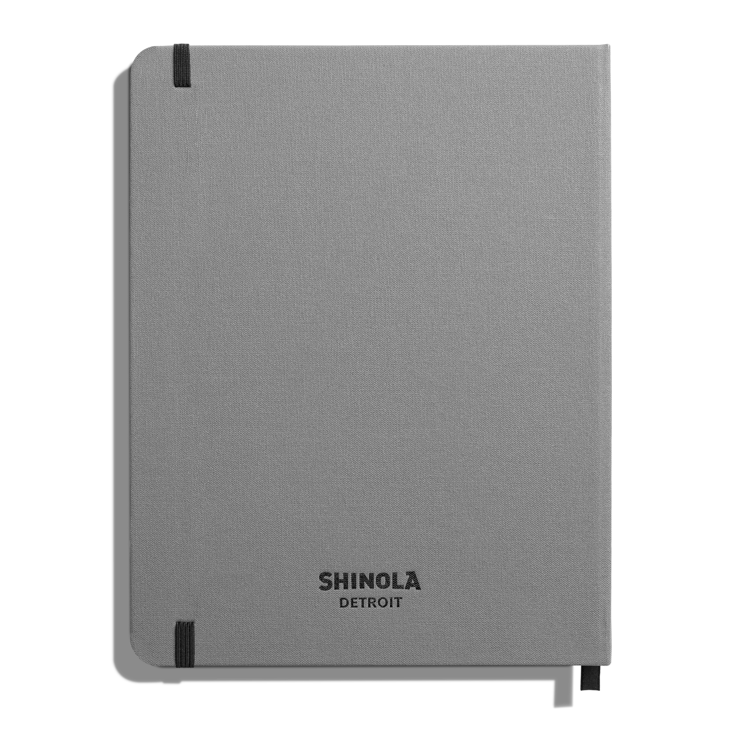 The Large Hard Grid Journal - Stone by Shinola is a closed, light gray hardcover notebook with smyth-sewn binding and black elastic bands on two corners. "SHINOLA DETROIT" is printed in black near the bottom of the cover.