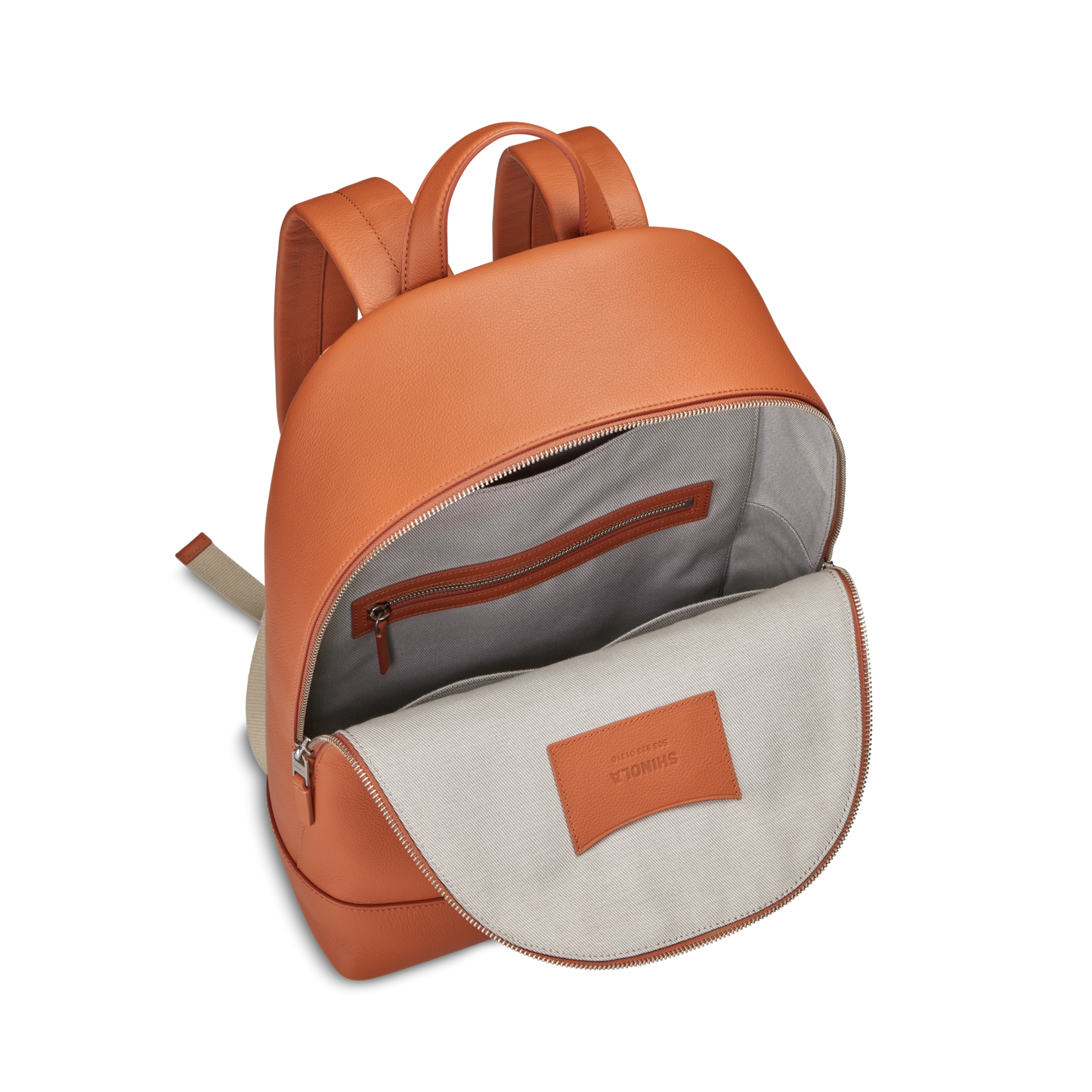 The Shinola Canfield Backpack in Rust features orange leather with a beige interior, a zippered pocket, and a stitched label—ideal as a stylish laptop backpack for travel or daily use.