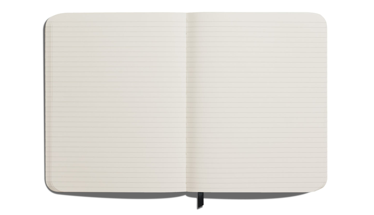 The Shinola Large Hard Ruled Journal in Navy, featuring acid-free lined pages and a black ribbon bookmark, lies flat on a white surface. Its elegant hard linen cover adds a sophisticated touch.