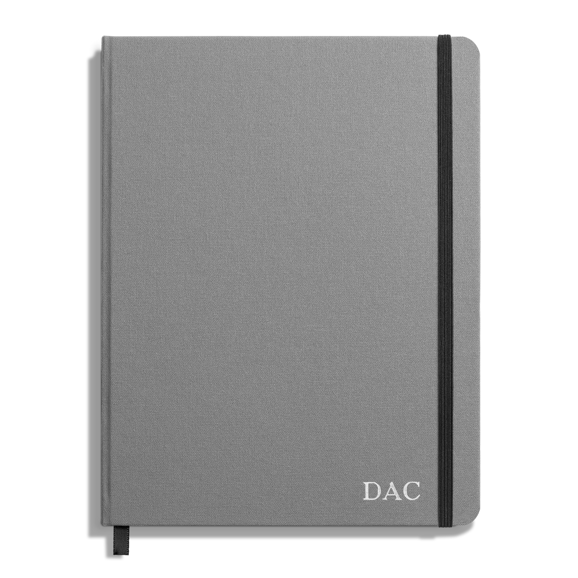 A closed Shinola Large Hard Ruled Journal in stone gray linen with a black elastic band on the right edge and the initials DAC printed in white on the bottom right corner of the cover.