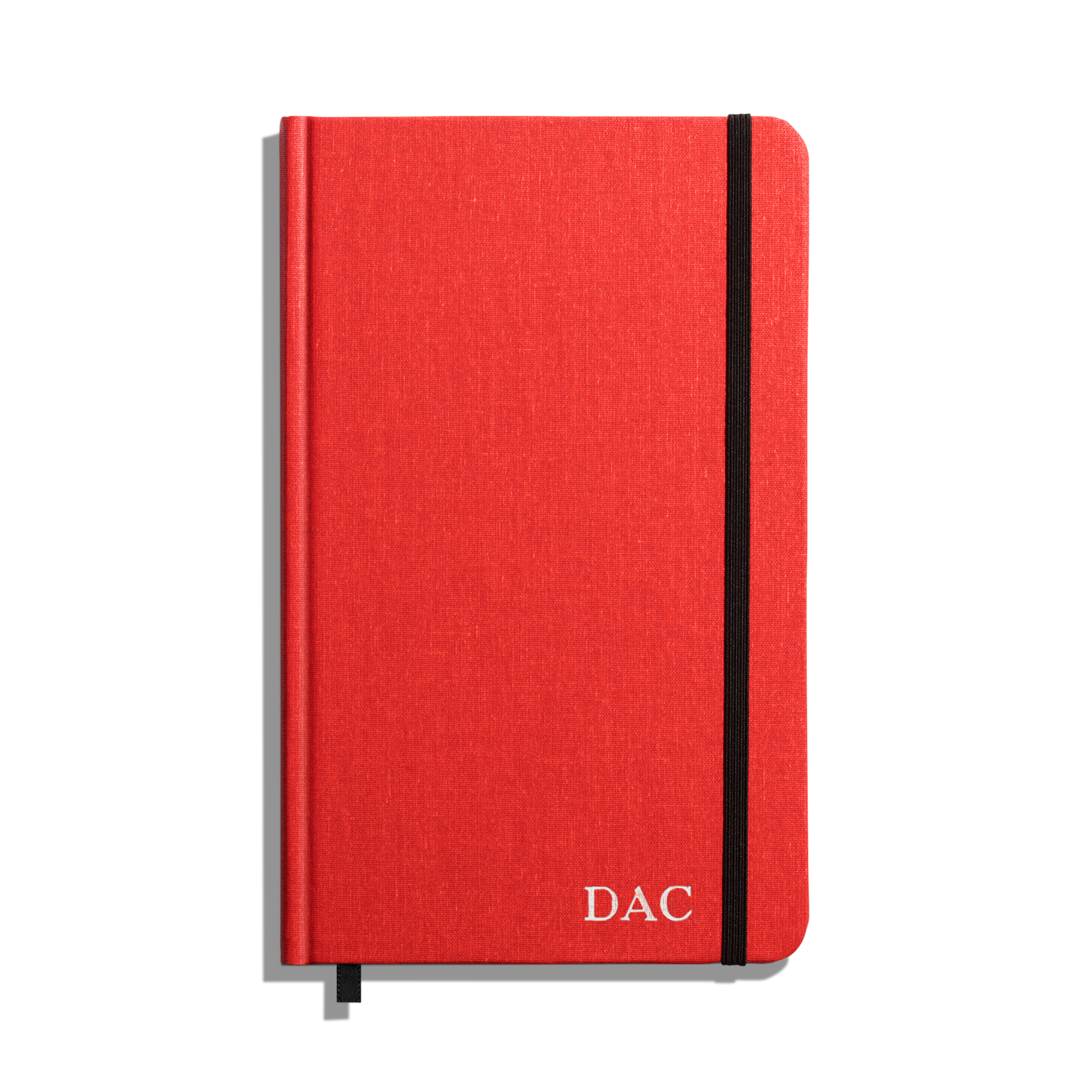 The Shinola Medium Hard Ruled Journal - Tomato is a red hardcover notebook with acid-free paper, black elastic band, black ribbon bookmark, and white DAC initials on the bottom right corner of the cover.