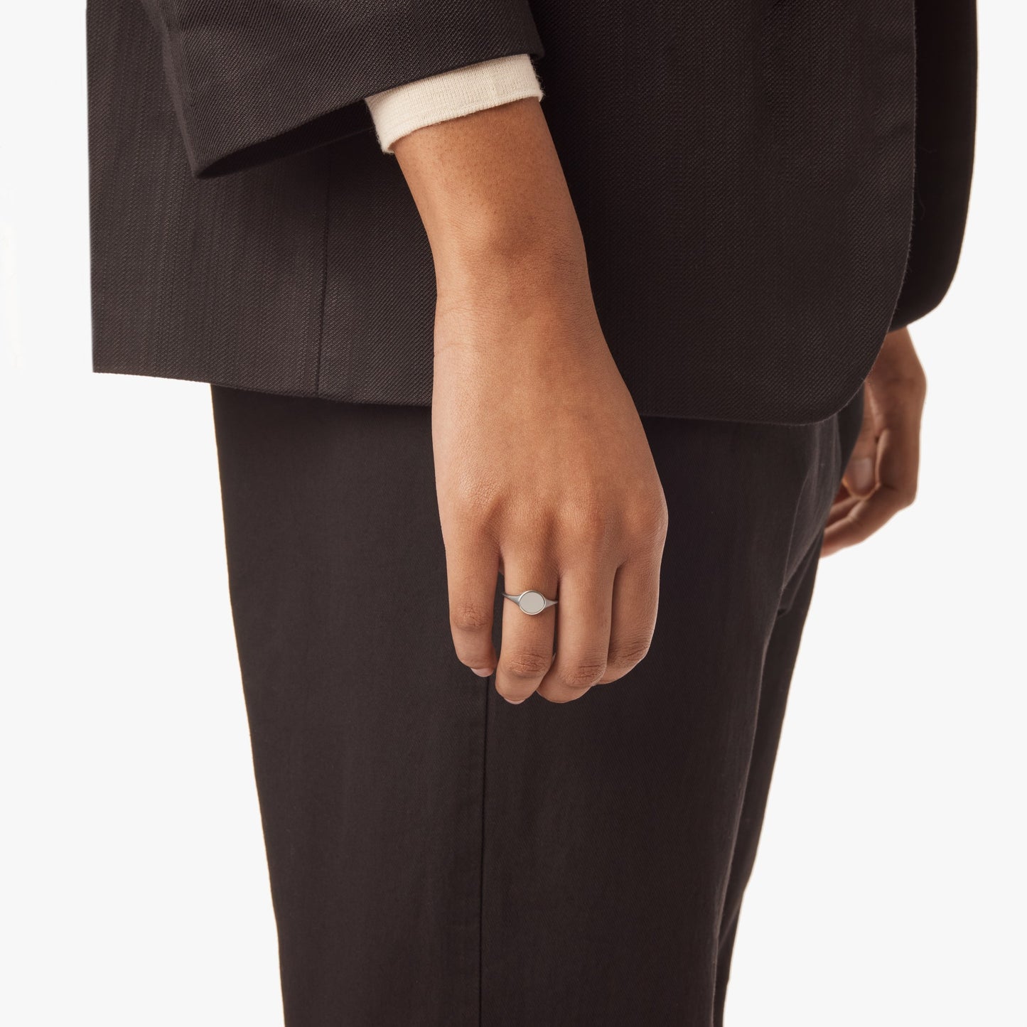 A person in a black suit and white shirt is shown from the waist down, their left hand relaxed by their side and wearing Shinola’s Petite Round Signet Ring - Sterling Silver for a timeless touch.